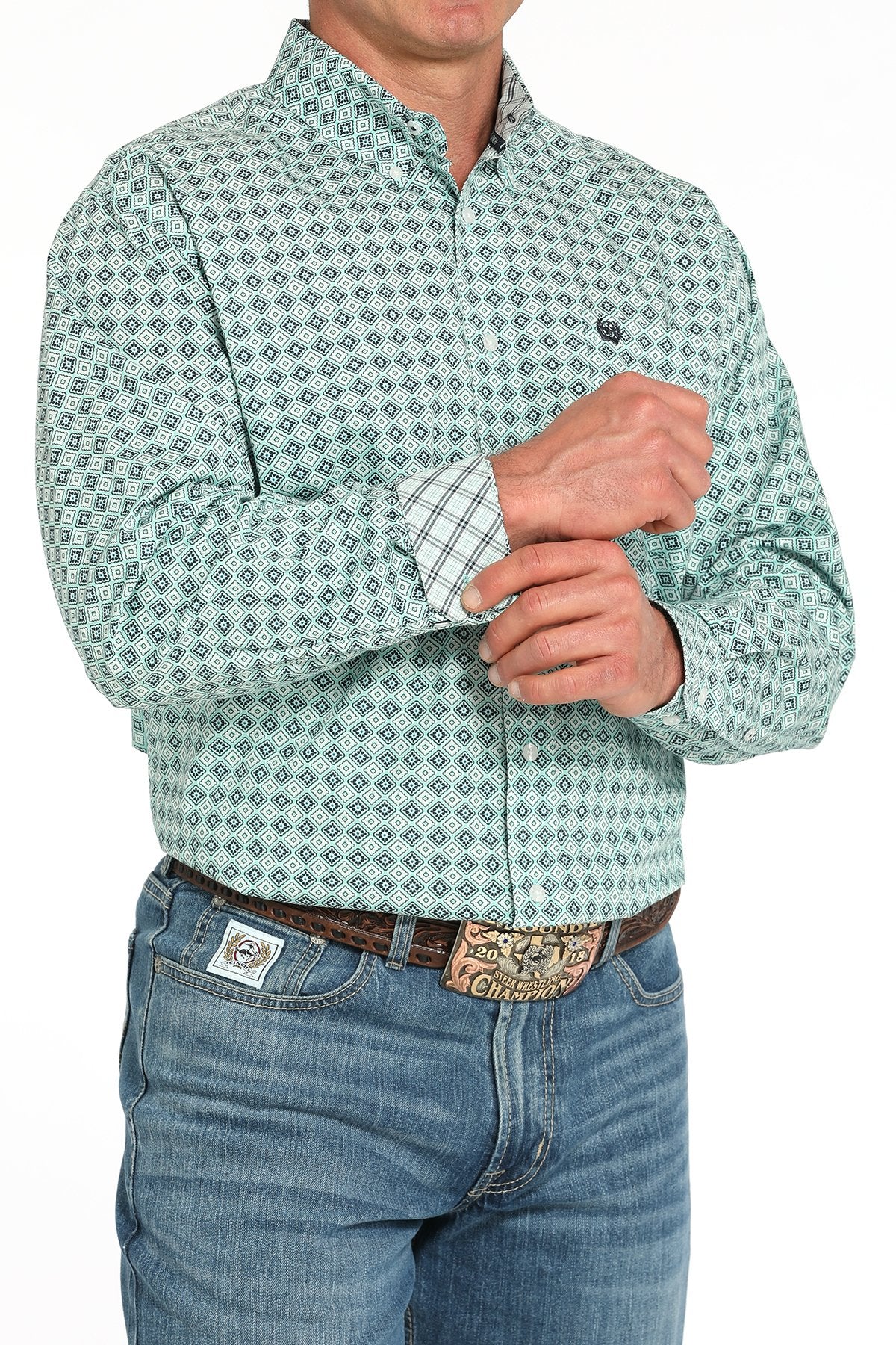 Side angled view of a man wearing a turquoise long-sleeve button-down shirt with a medallion print pattern, paired with blue jeans and a western belt buckle displayed on a white background.