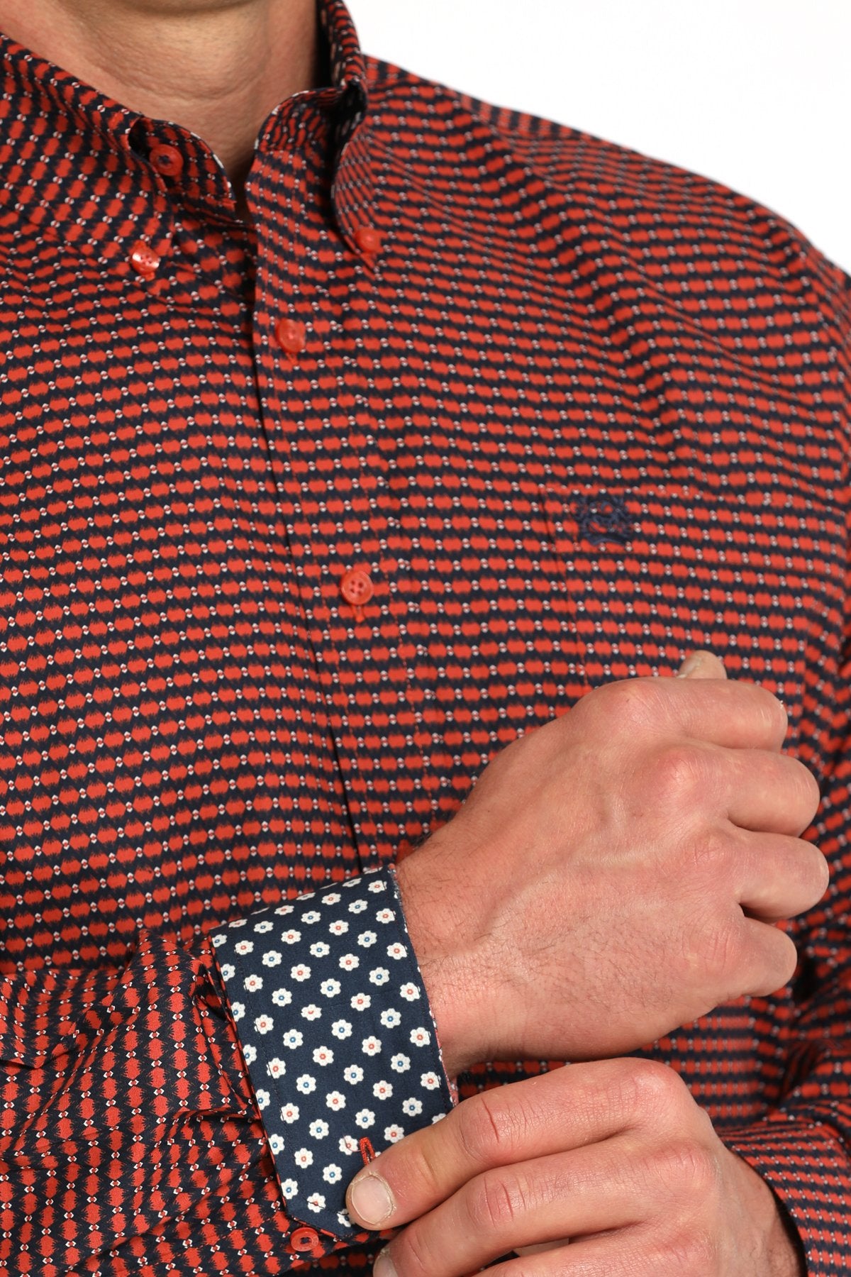 Close-up view of a man wearing a red patterned button-down shirt with contrasting navy floral print on the inside cuff displayed on a white background.