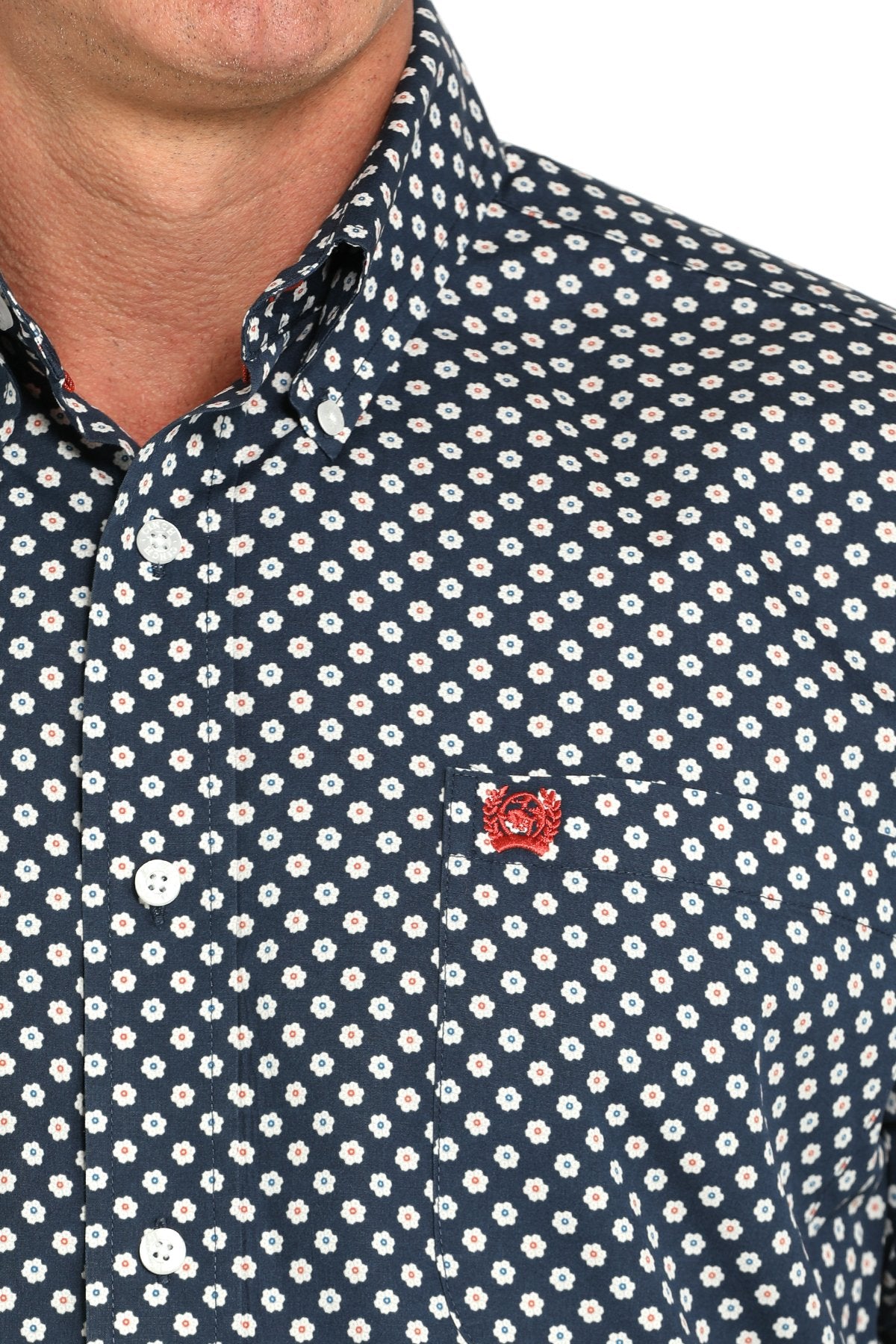 Close-up view of a navy long-sleeve button-down shirt with a white daisy print pattern and red chest logo displayed on a white background.