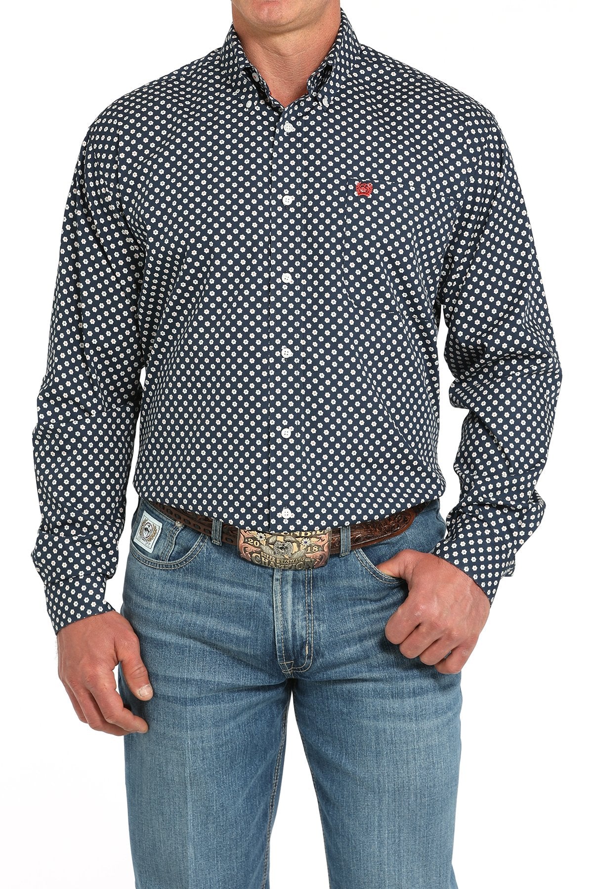 Front view of a man wearing a navy long-sleeve button-down shirt with a white daisy print pattern and a red chest logo, paired with blue jeans and a western belt buckle displayed on a white background.