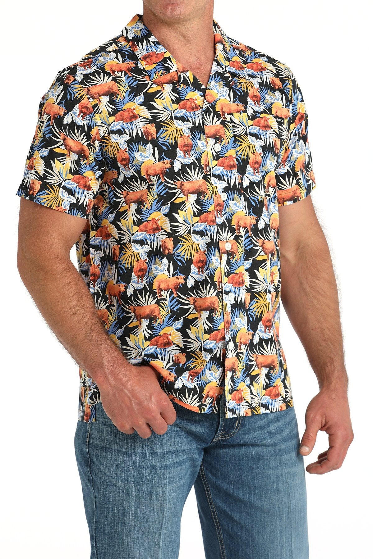 Side angled view of a man wearing a multicolor tropical print short-sleeve button-down shirt, paired with blue jeans displayed on a white background.