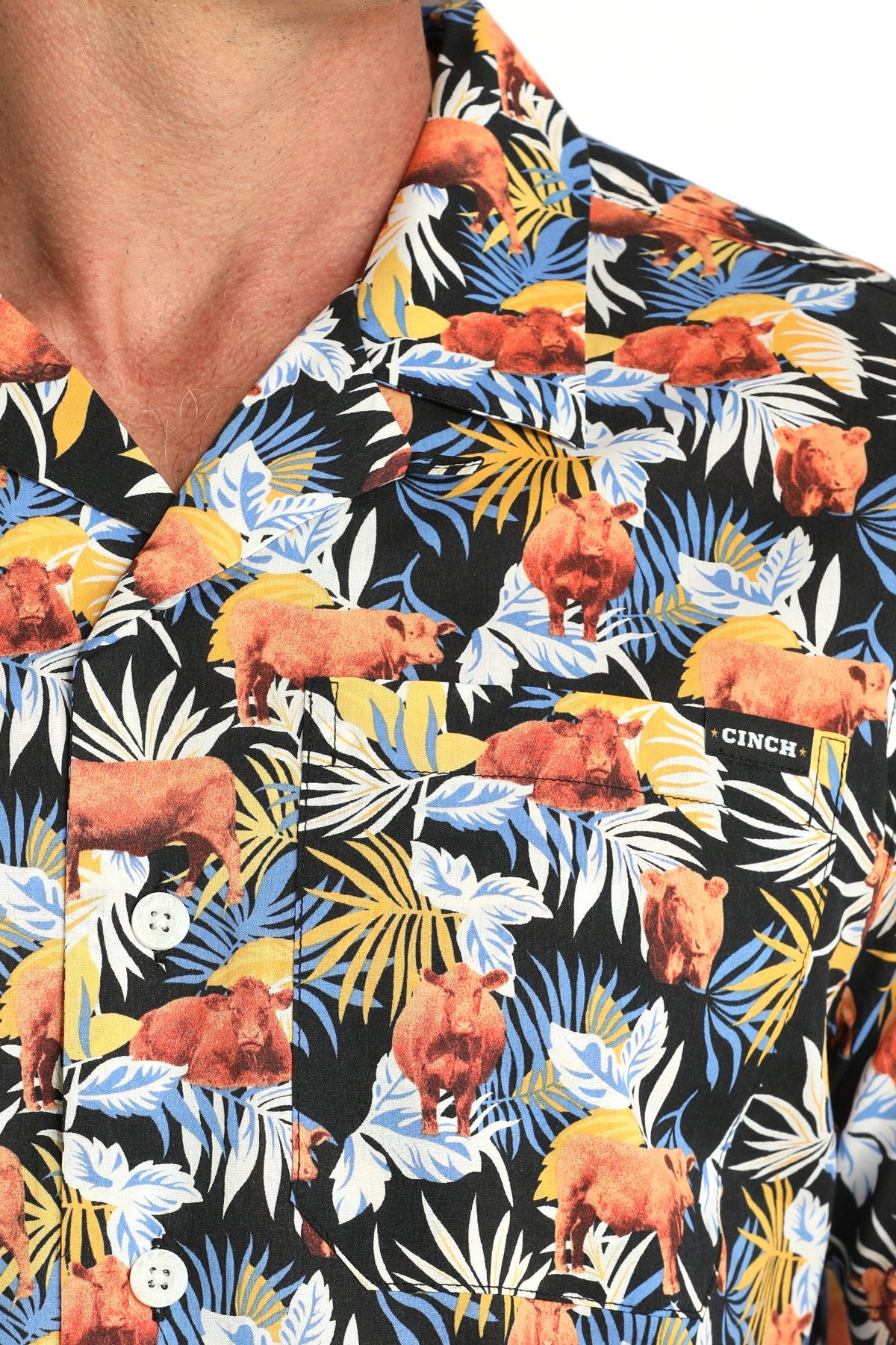 Close-up view of a multicolor tropical print short-sleeve button-down shirt with orange, yellow, and white floral patterns displayed on a white background.