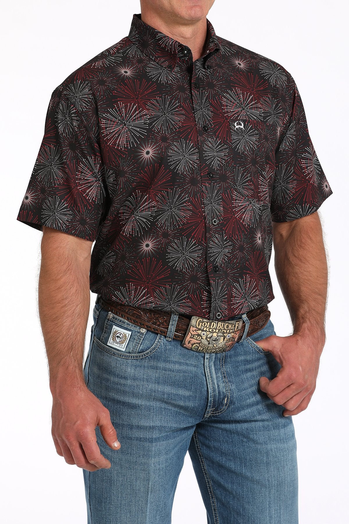 Side angled view of a man wearing a black short-sleeve button-down shirt with a fireworks pattern, paired with blue jeans and a western belt buckle displayed on a white background