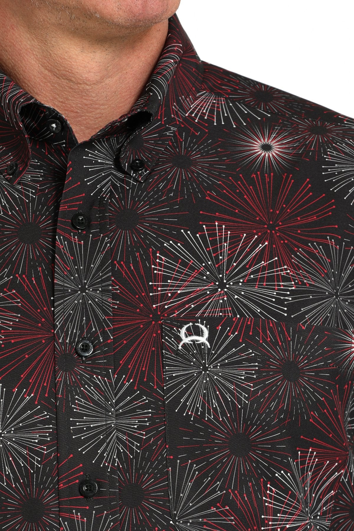Close-up view of a black short-sleeve button-down shirt with a red and gray fireworks pattern and a small logo displayed on a white background.