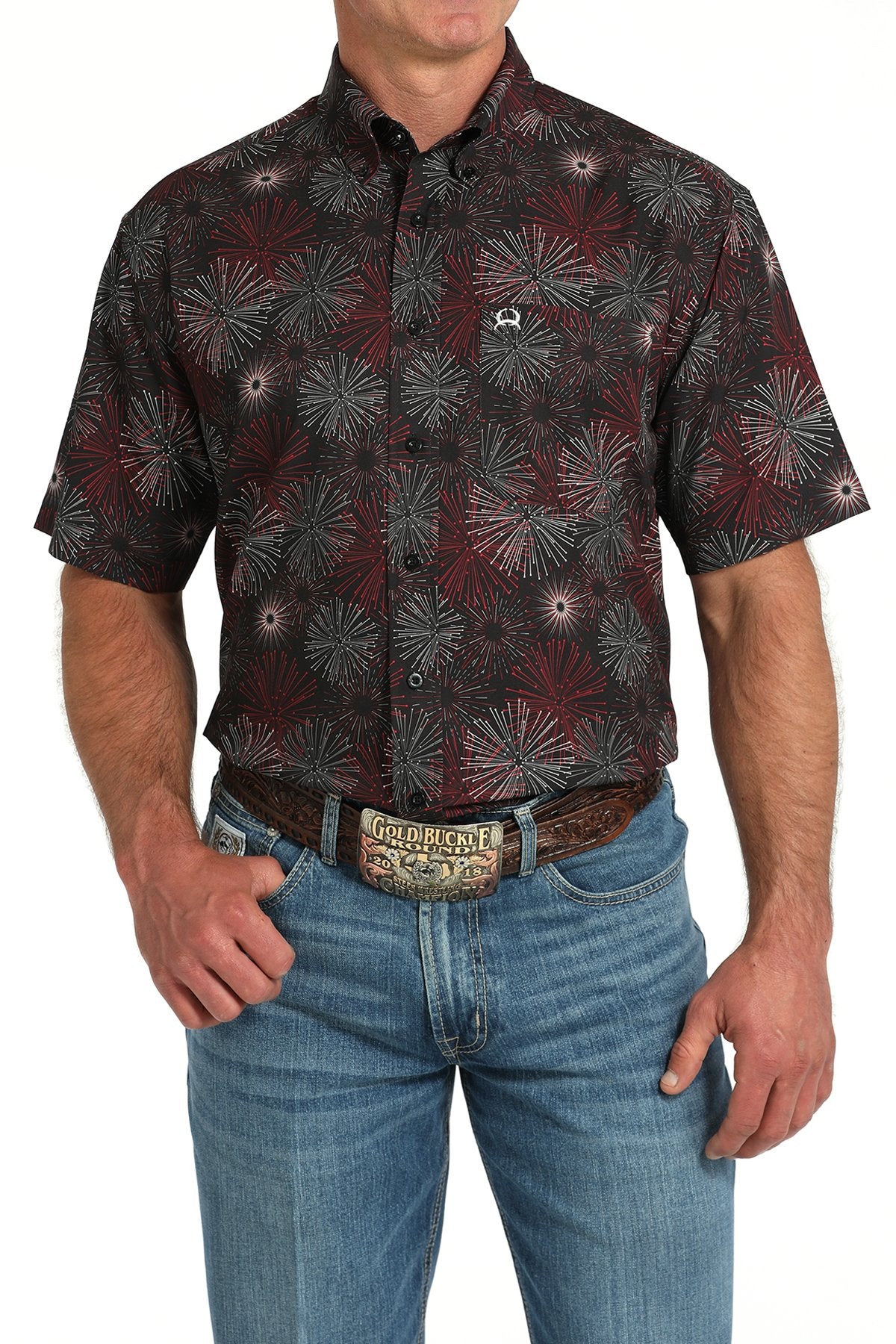 Front view of a man wearing a black short-sleeve button-down shirt with a red and gray fireworks pattern, paired with blue jeans and a western belt buckle displayed on a white background.