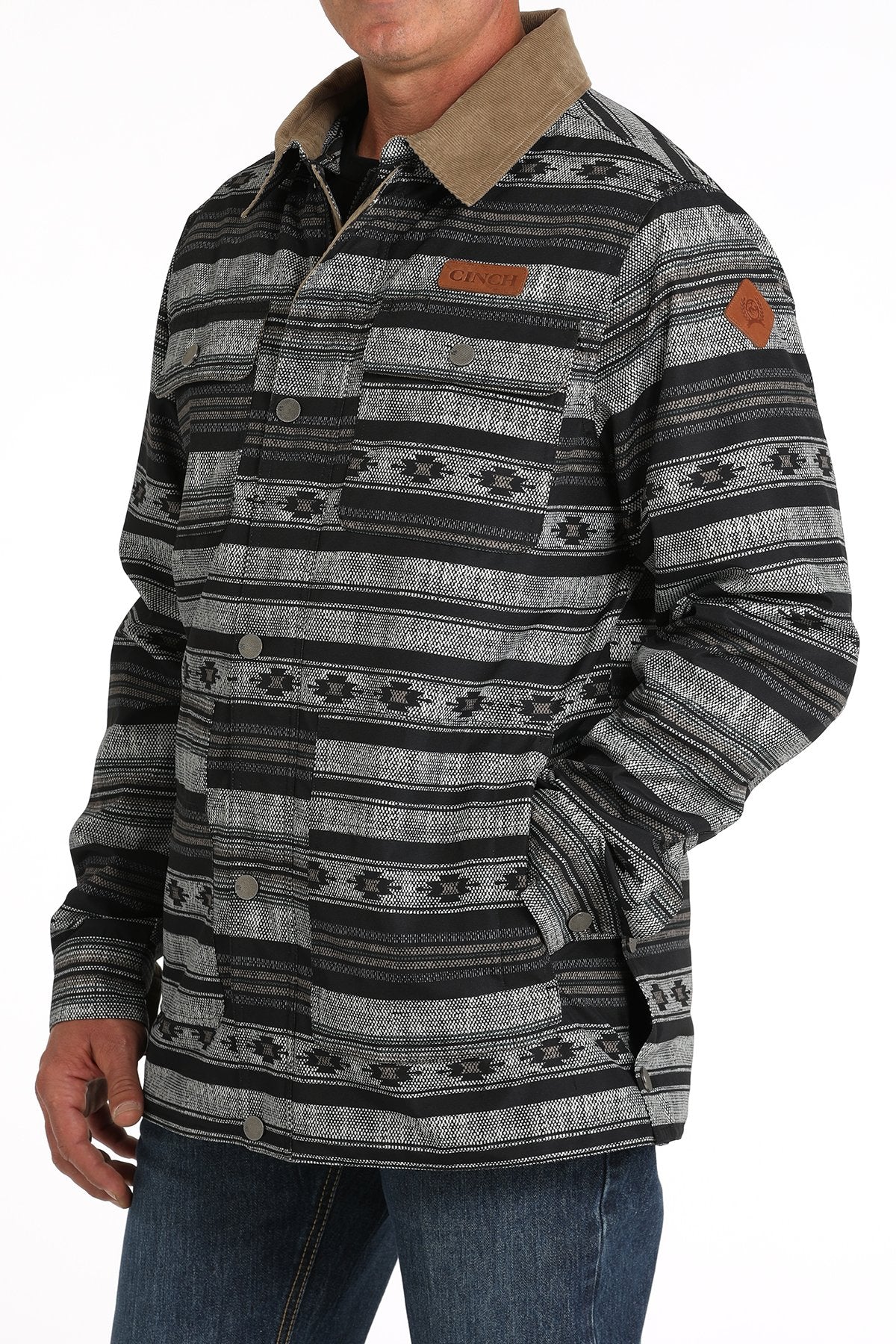 Man wearing a black and gray patterned button-up jacket with a hood and blue jeans displayed on a white background.