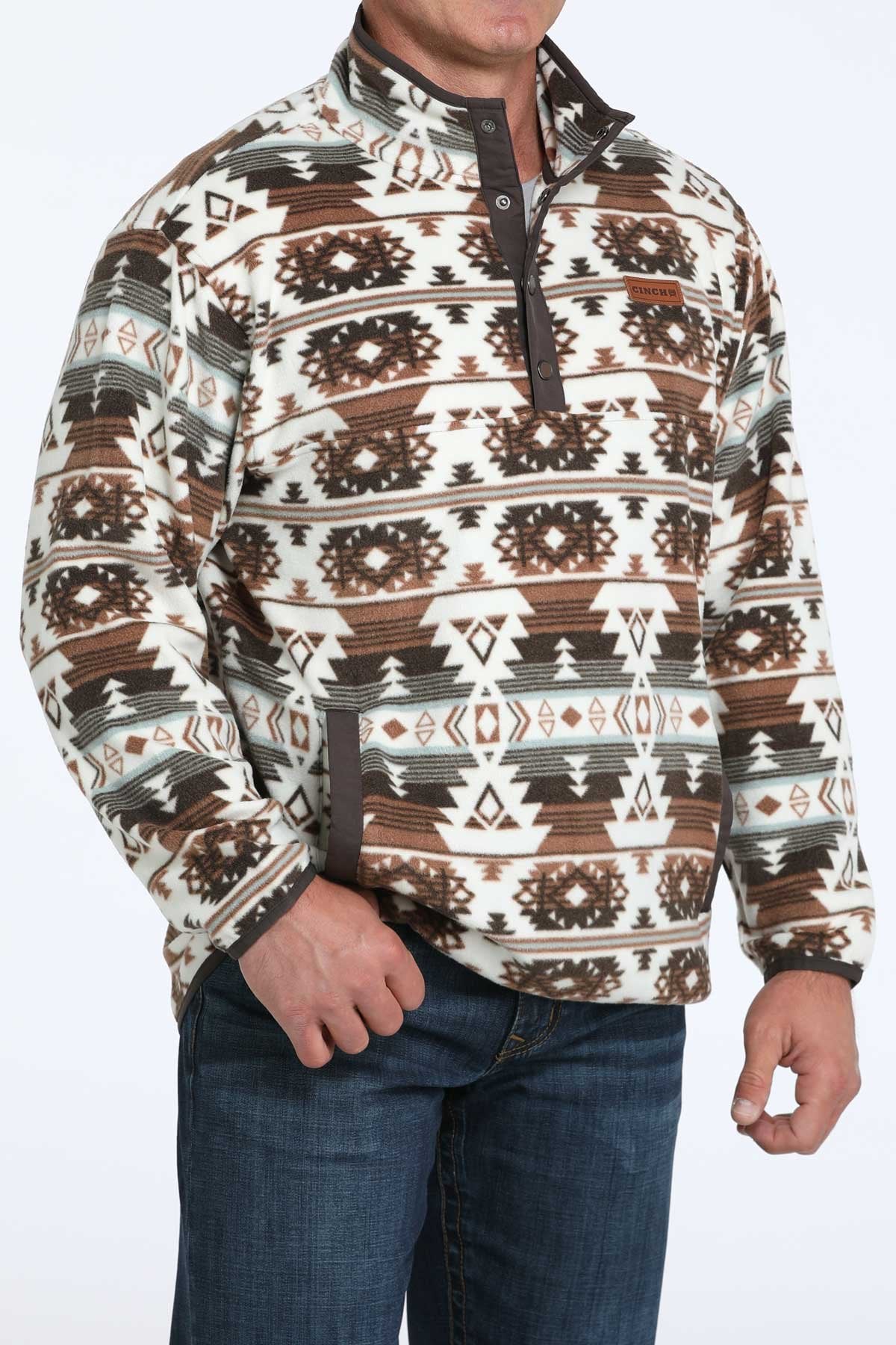 Side angled view of a man wearing a brown and white Southwestern patterned quarter-zip pullover with blue jeans displayed on a white background.