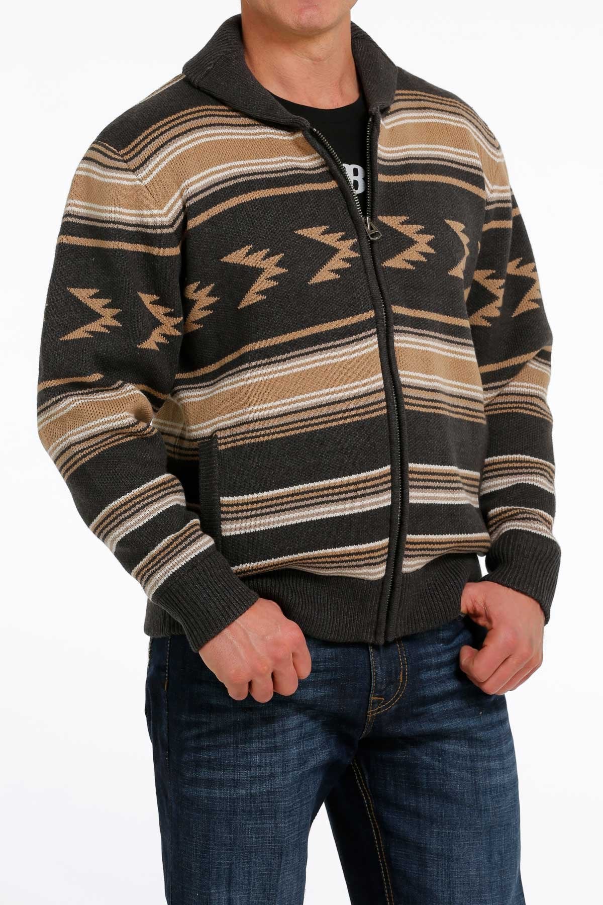 Man wearing a brown and black patterned zip-up sweater jacket with blue jeans displayed on a white background.