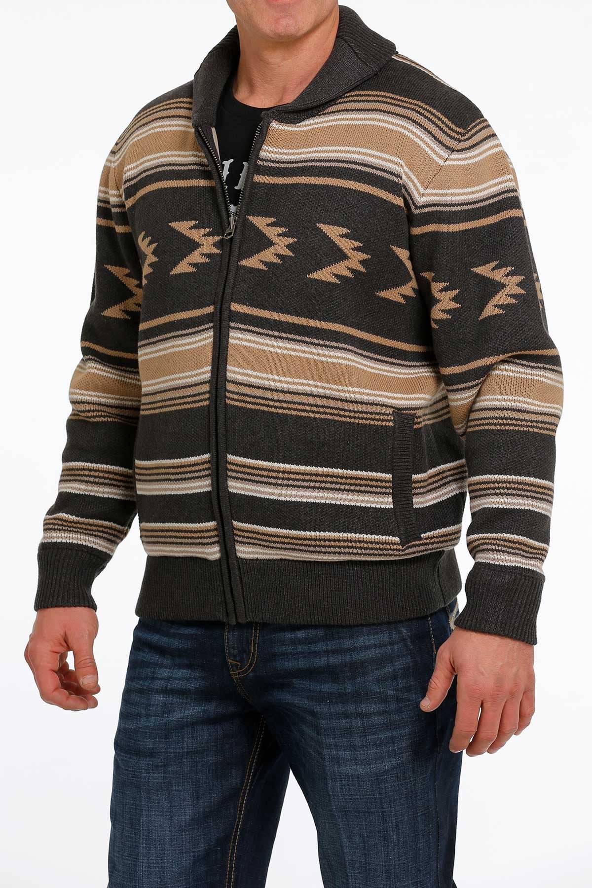 Man wearing a brown and black patterned zip-up sweater jacket with blue jeans displayed on a white background.