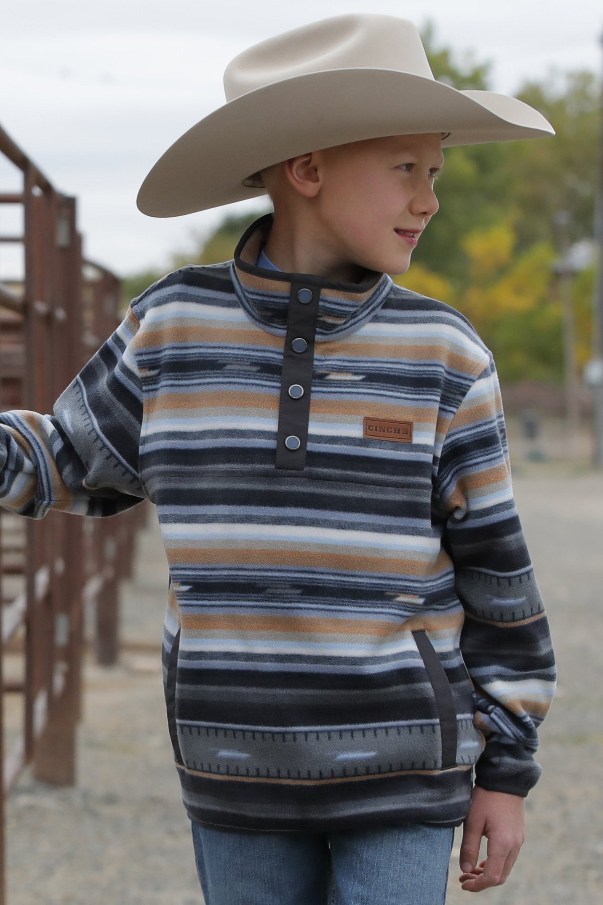 Boy standing outside wearing a pullover jacket and jeans with a cowboy hat