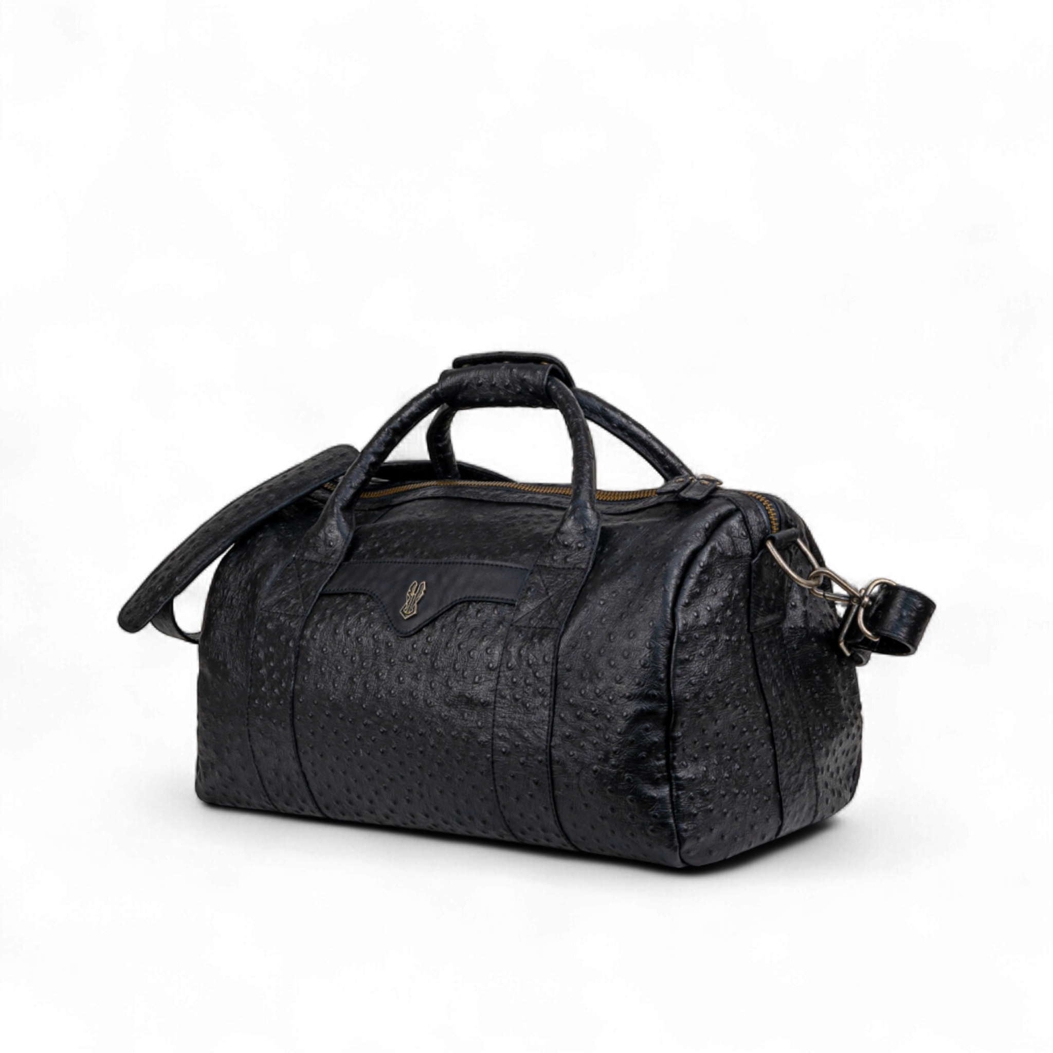 Black ostrich-print duffel bag with dual top handles, a detachable shoulder strap, and a gold zipper. A small metallic emblem is featured on the front center panel