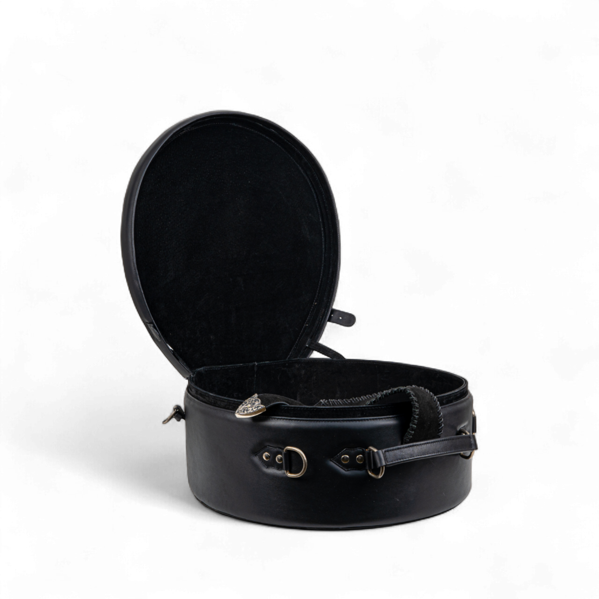 Black tooled leather hat case shown open, revealing a spacious, round interior with a soft lining. The exterior features a silver buckle accent, side rings, and a sturdy carrying strap