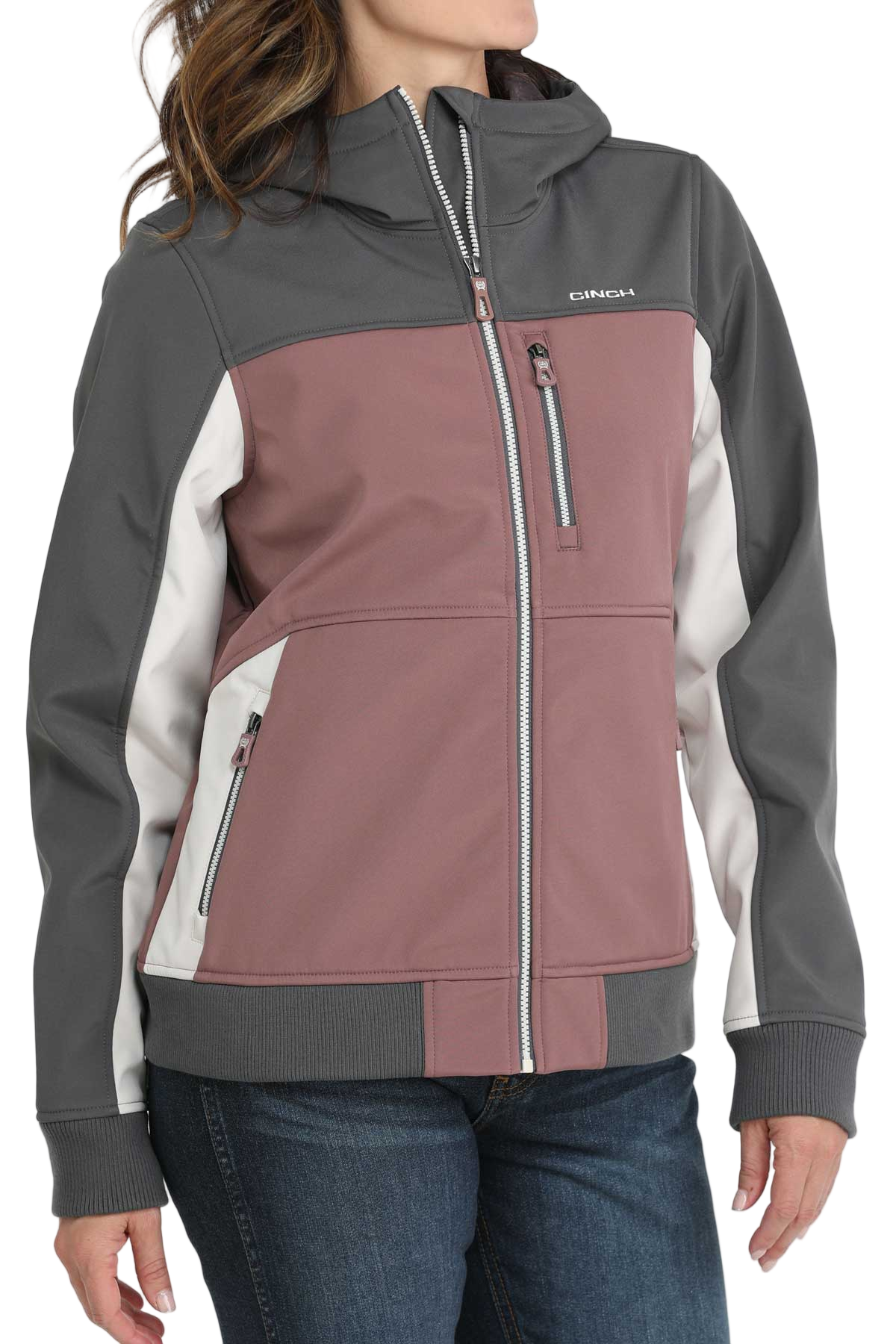 A woman wearing a color-blocked jacket with mauve, gray, and white panels, paired with blue jeans