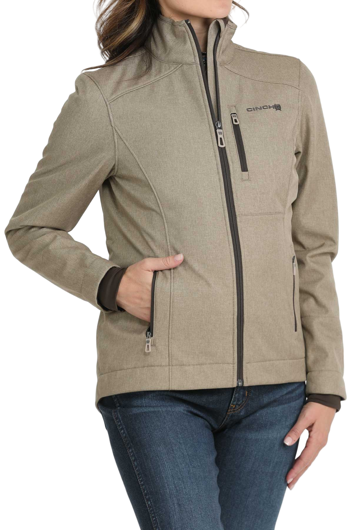 A woman wearing a light olive zip-up jacket with a high collar and front pockets, paired with dark jeans 