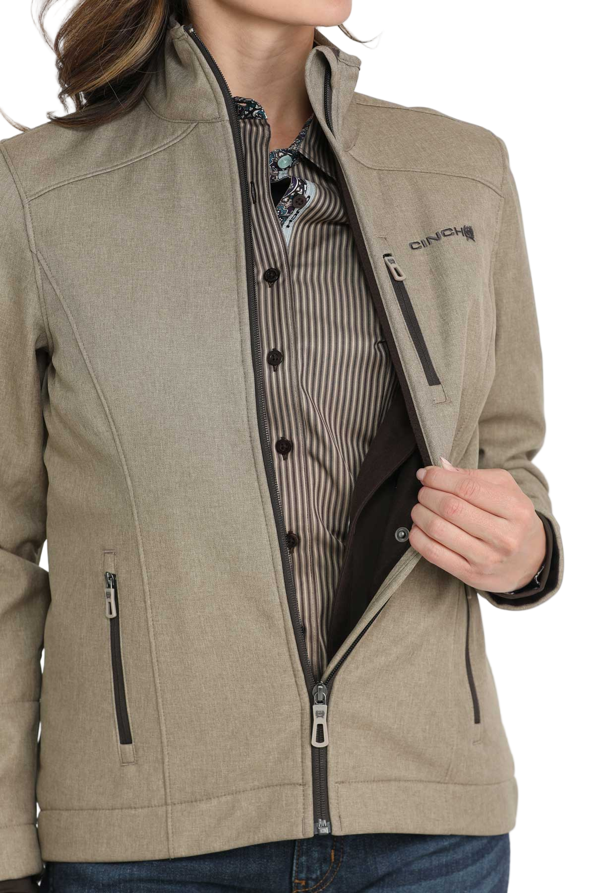 A woman unzipping a light olive jacket to show the striped shirt underneath, with one hand holding the jacket open