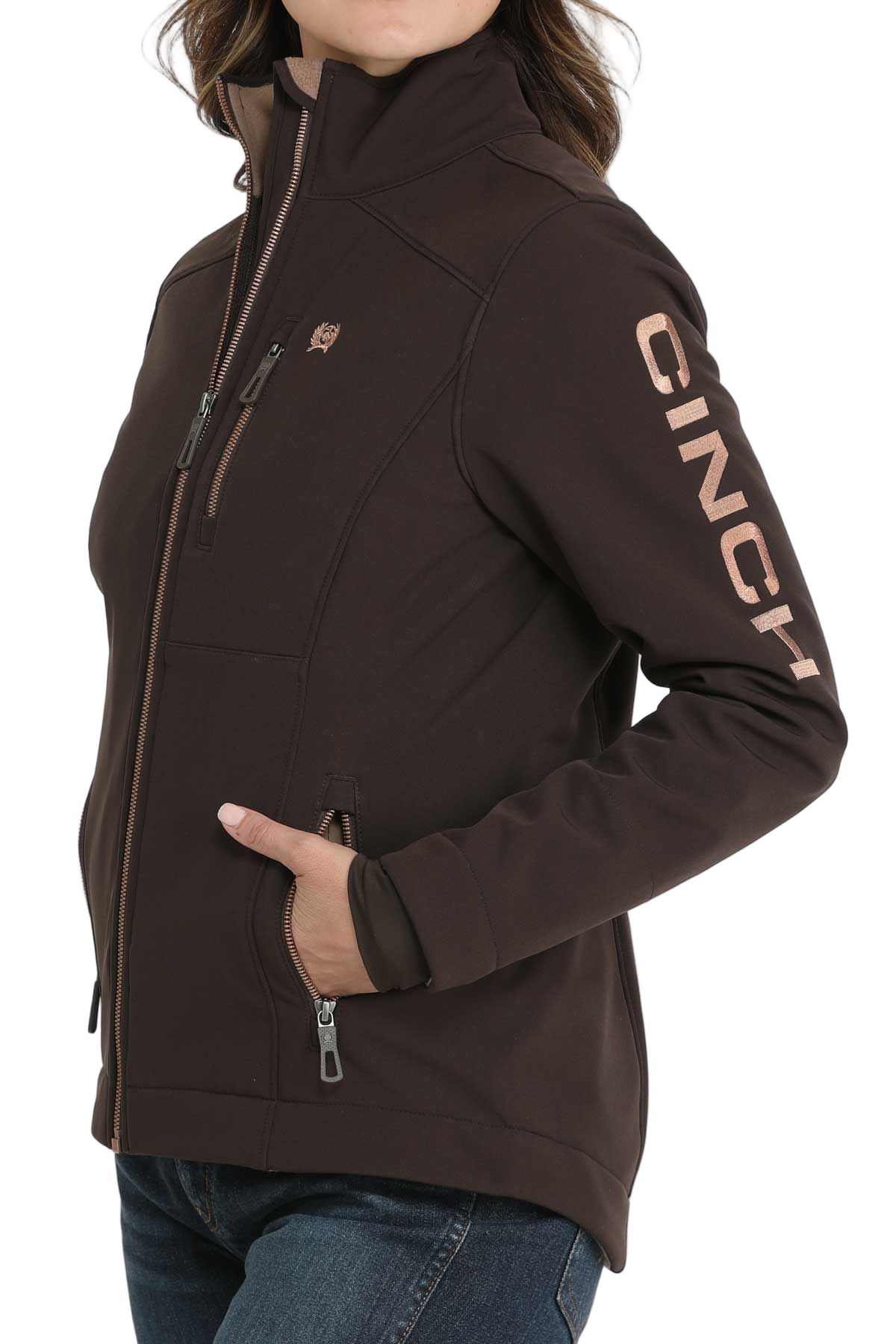 Woman wearing a dark brown CINCH softshell jacket with a front zipper and jeans, shown from the side