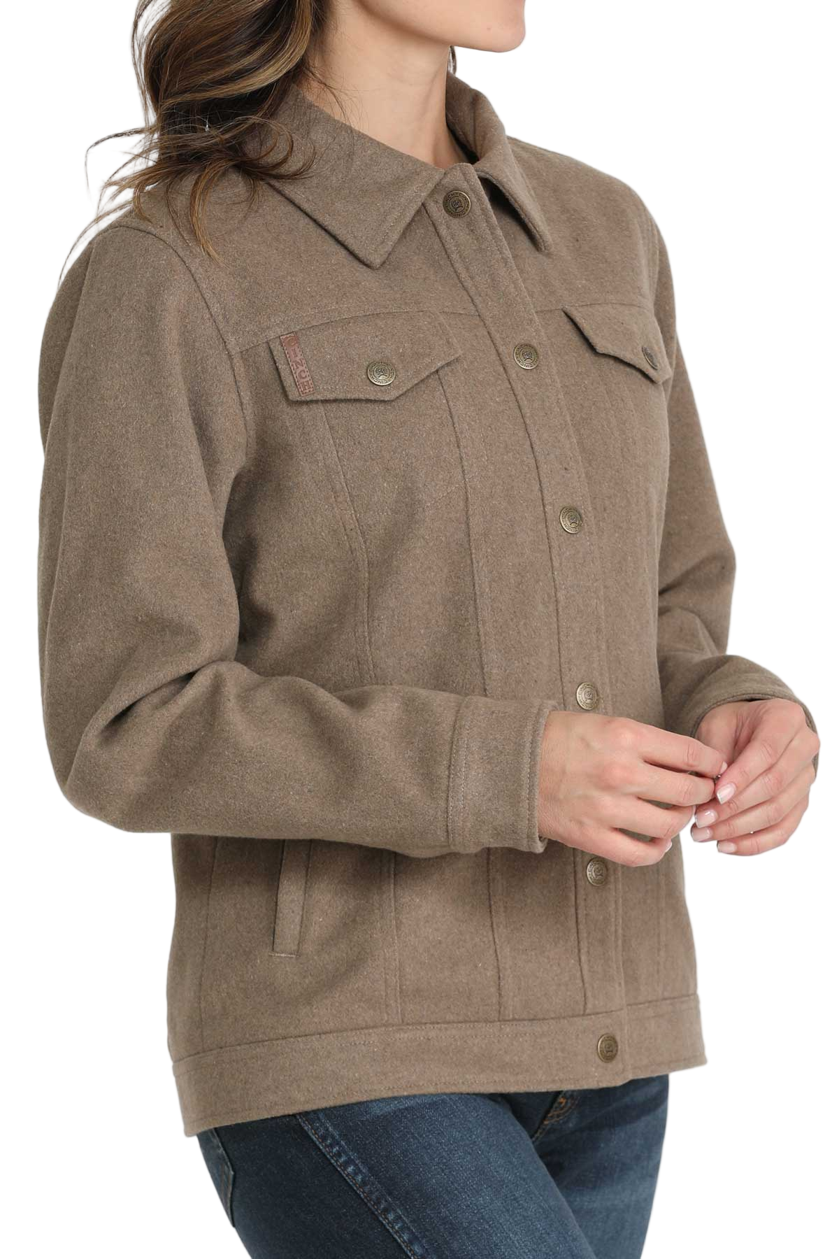 A woman wearing a taupe button-up jacket with flap chest pockets and long sleeves, paired with blue jeans