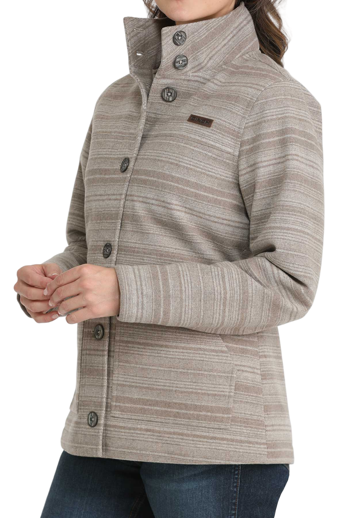 Woman wearing a beige patterned button-up jacket with a high collar, paired with dark blue jeans