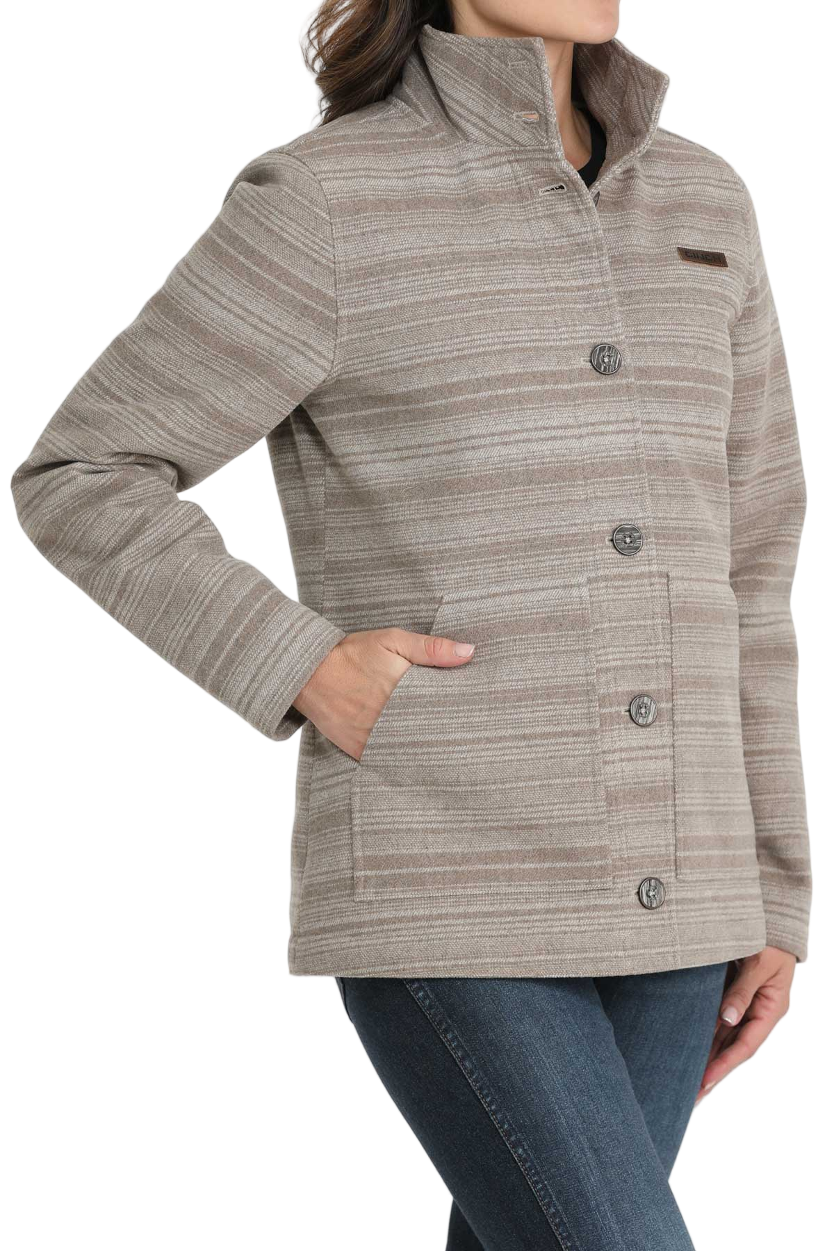 Woman wearing a beige patterned button-up jacket with a high collar, paired with dark blue jeans