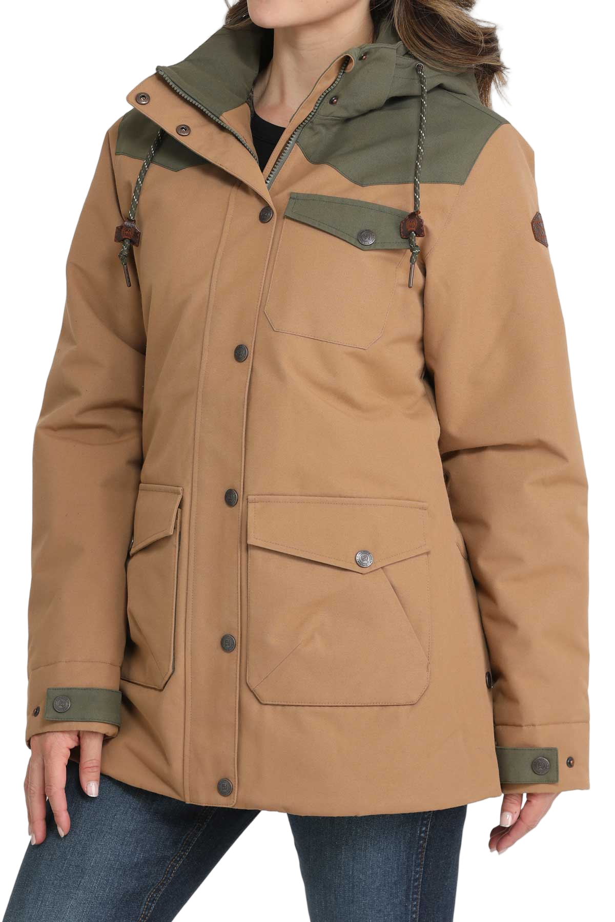 Woman wearing a tan and olive green hooded jacket with front pockets and button closures, paired with dark denim jeans
