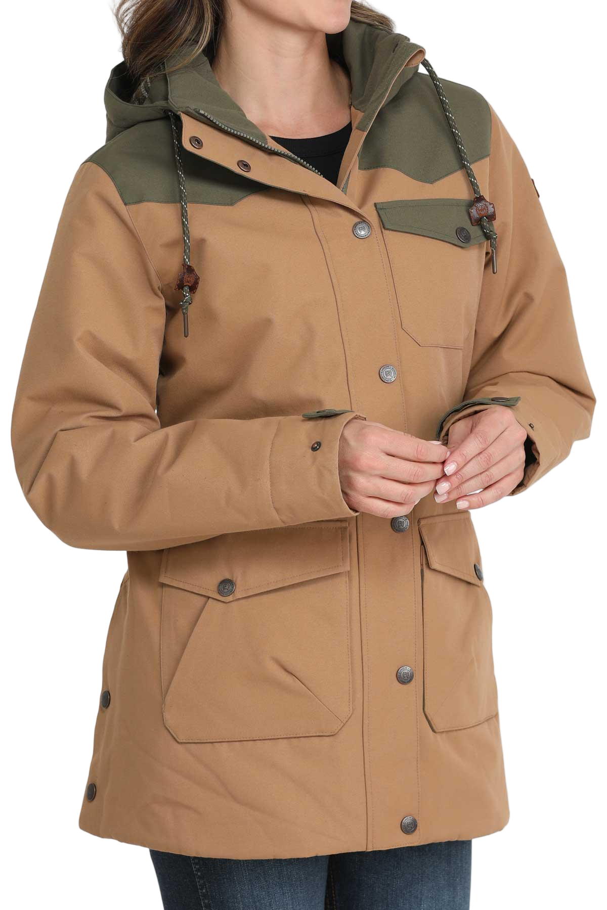 Woman wearing a tan and olive green hooded jacket with front pockets and button closures, paired with dark denim jeans