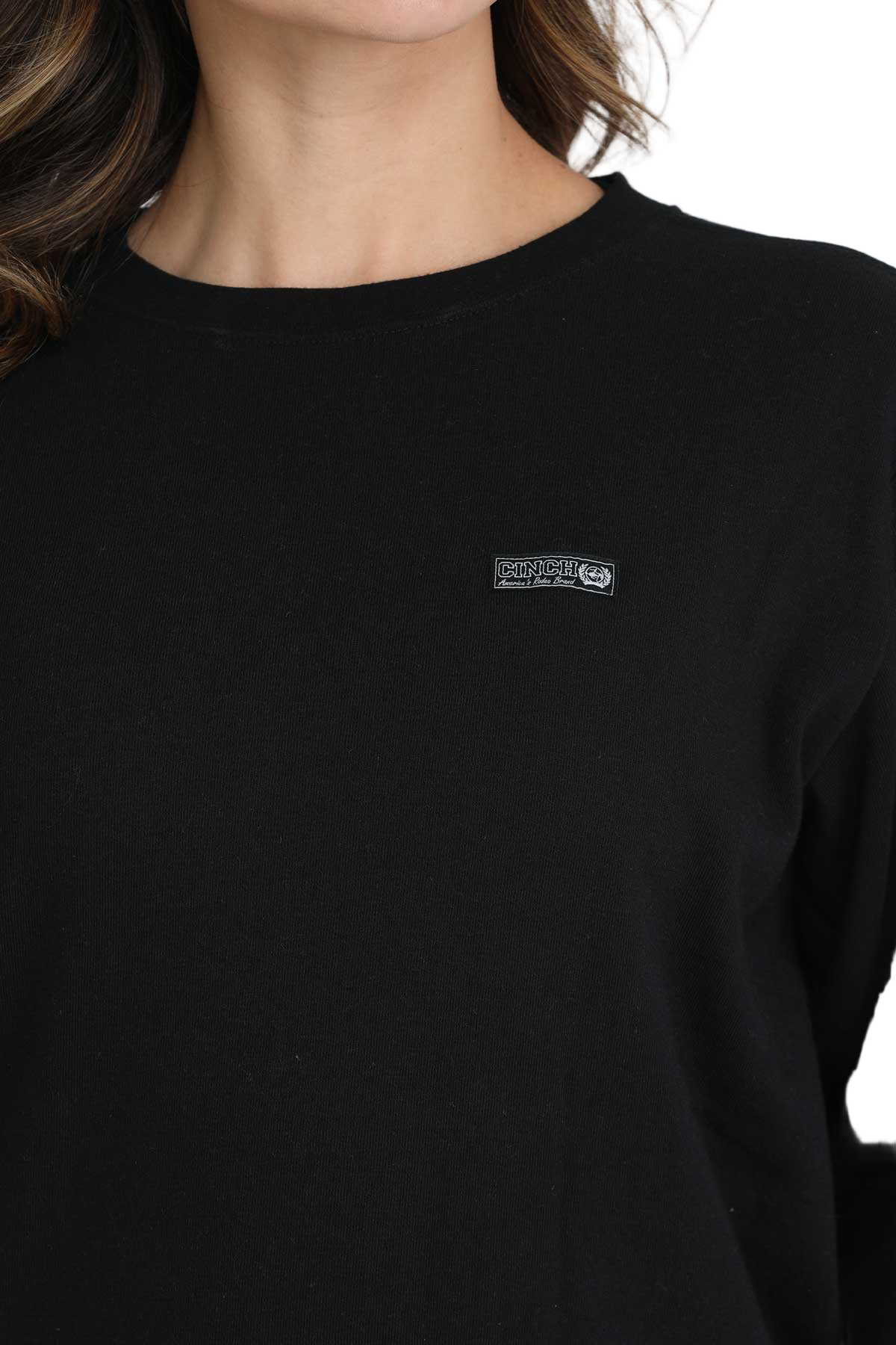 Close-up of a woman wearing a black crewneck sweatshirt with a small embroidered logo on the chest