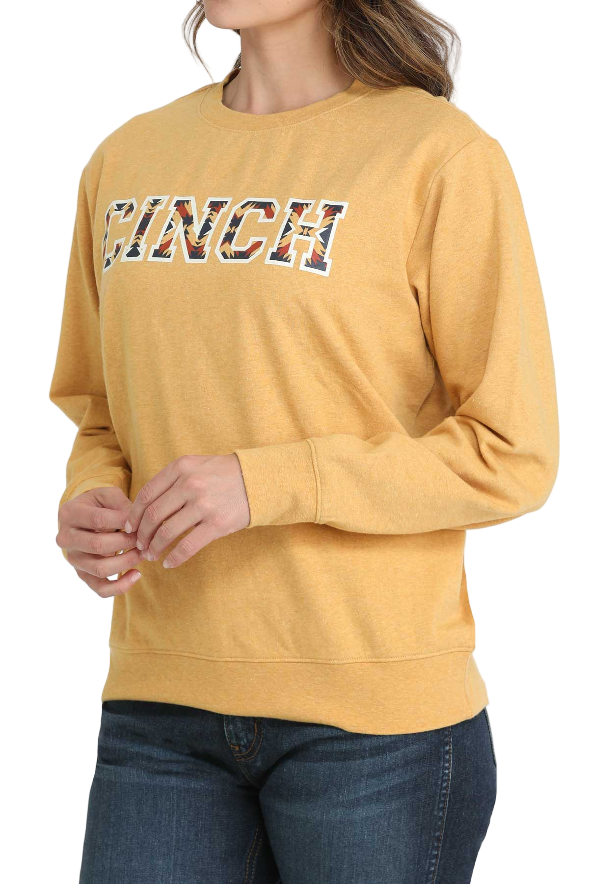 Woman wearing a yellow crewneck sweatshirt with patterned CINCH lettering, paired with dark-wash jeans