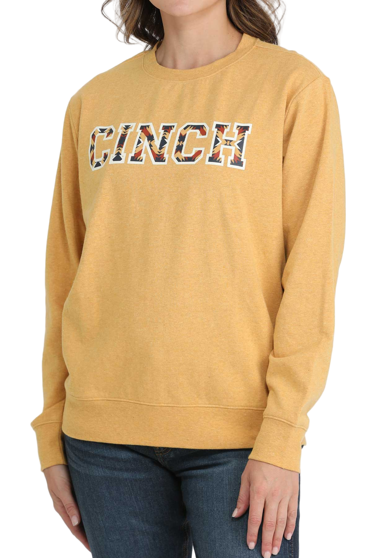 Woman wearing a yellow crewneck sweatshirt with patterned CINCH lettering, paired with dark-wash jeans