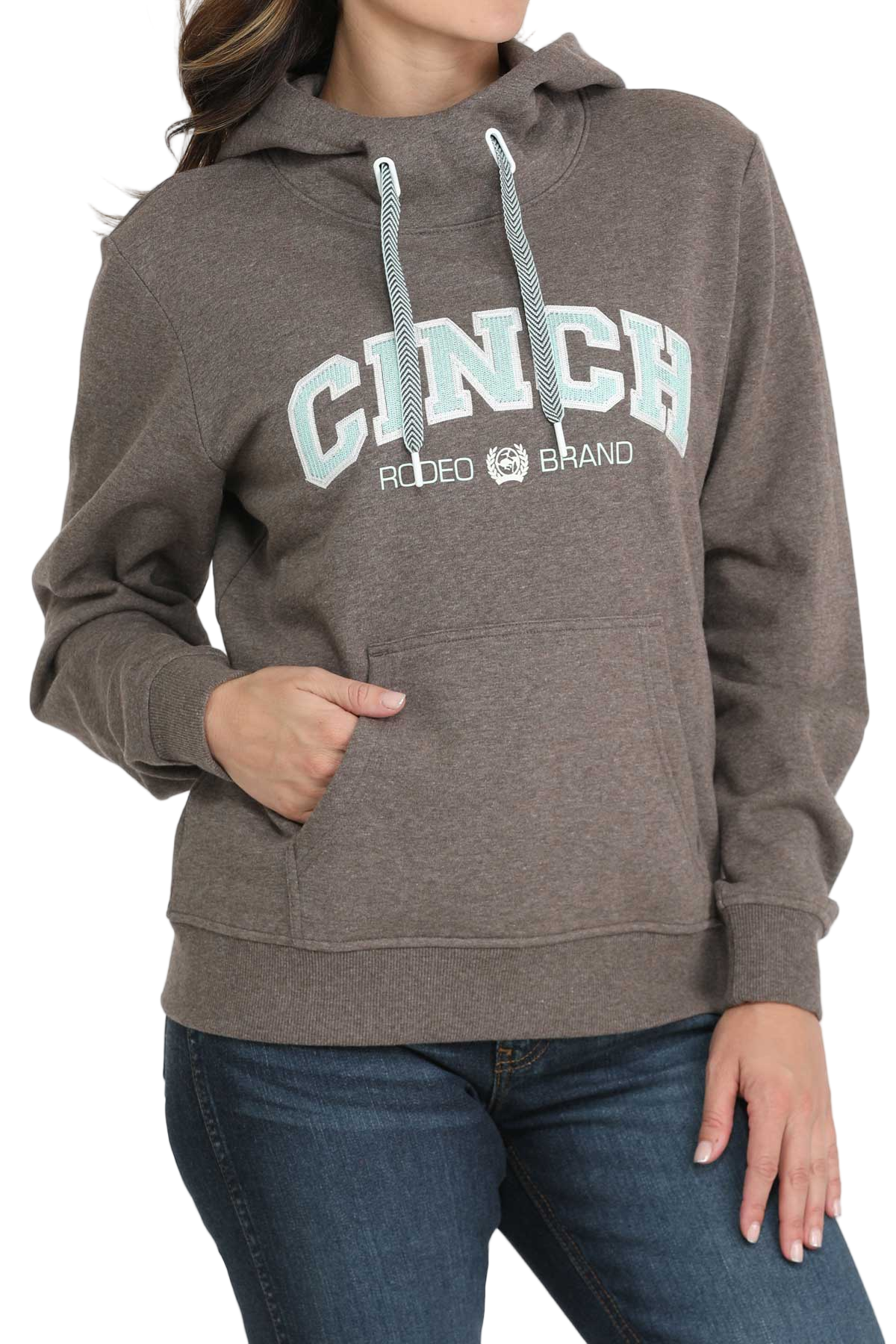 Woman wearing a brown CINCH hoodie with blue drawstrings and a front kangaroo pocket, paired with blue jeans