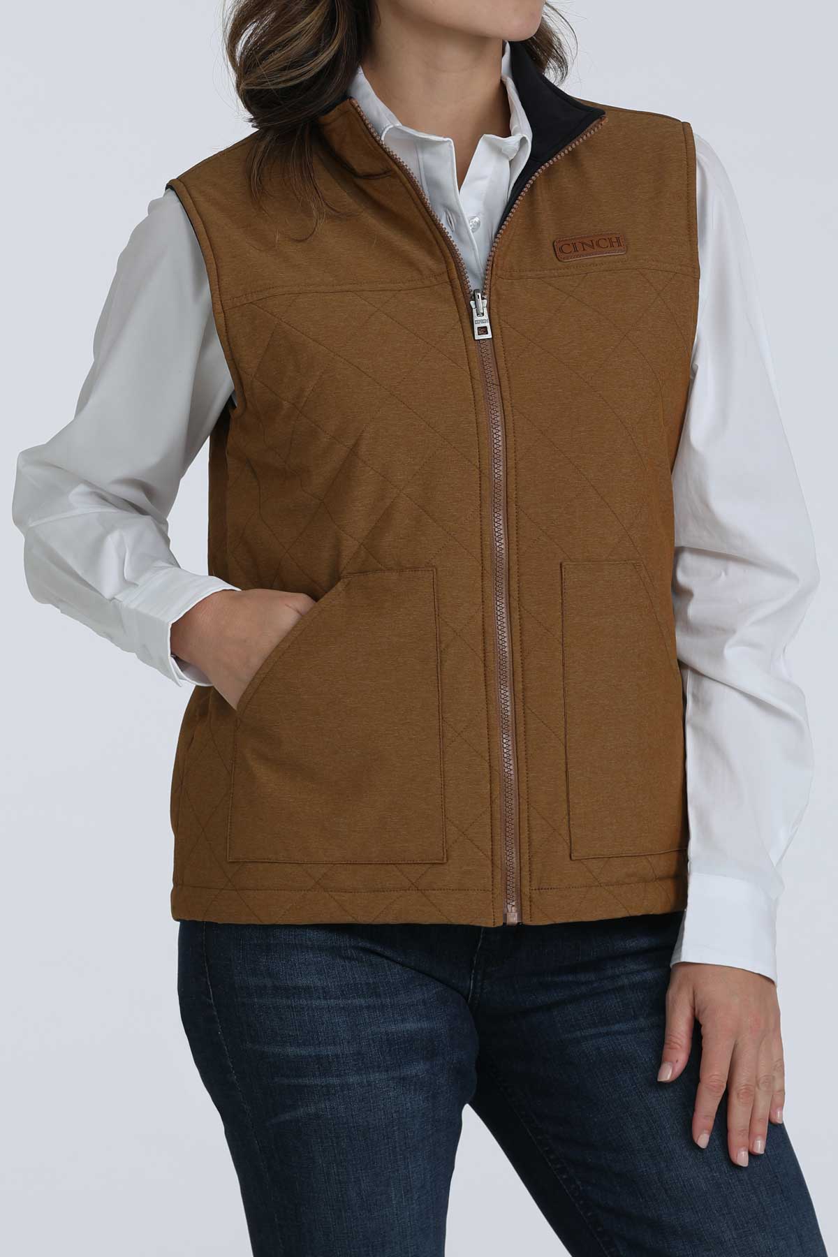 Woman wearing a brown vest with a white undershirt and jeans 