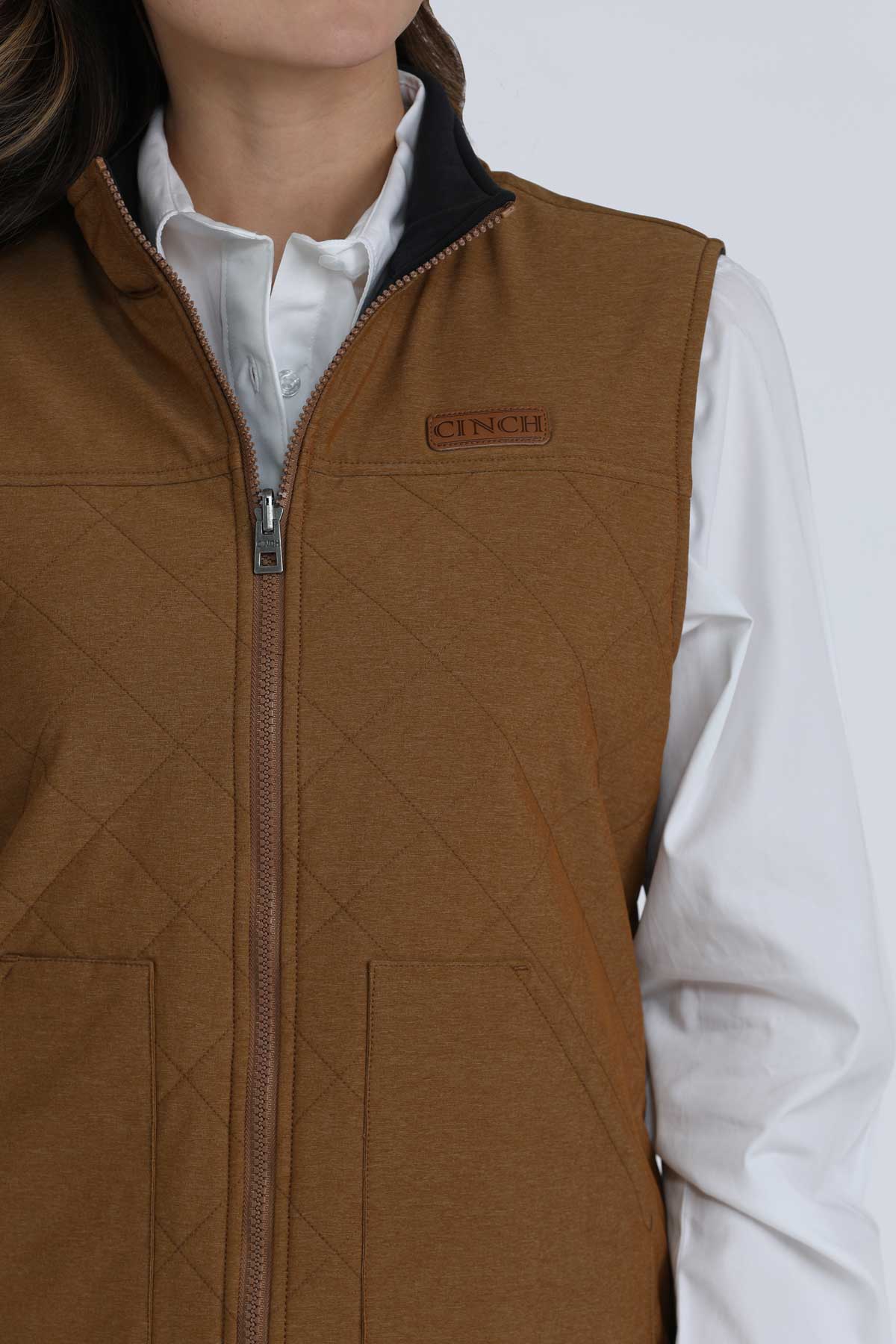 Close-up of a woman wearing a brown vest with a white undershirt 