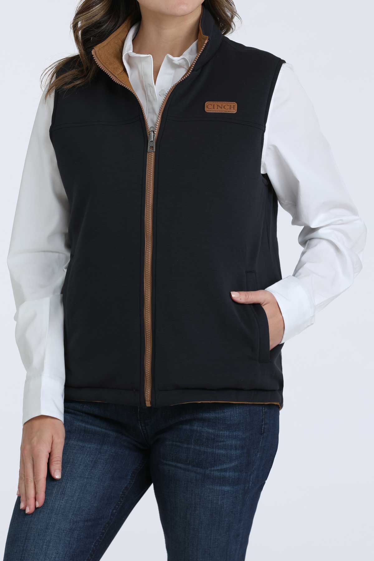 Woman wearing a black vest with a white undershirt and jeans 