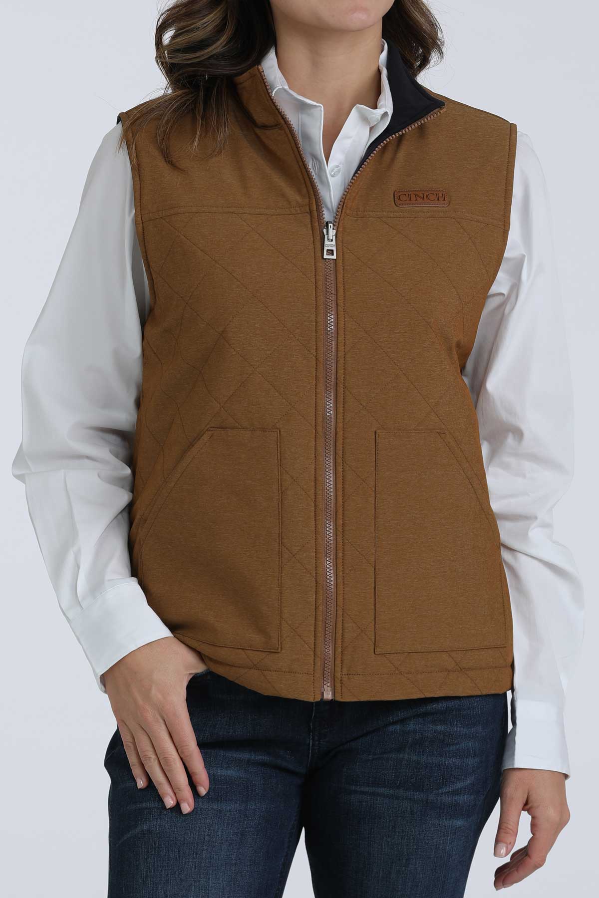 Woman wearing a brown vest with a white undershirt and jeans 