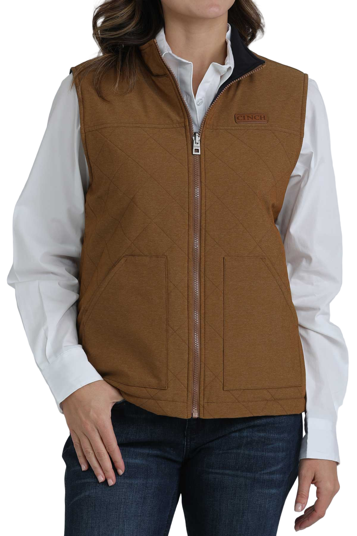 Woman wearing a brown quilted vest over a white button-up shirt and dark jeans 