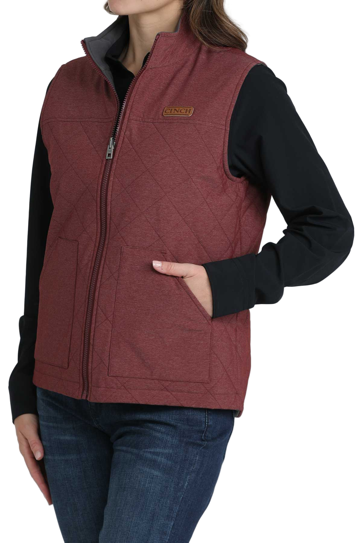 Woman wearing a quilted burgundy zip-up vest over a black long-sleeve shirt, paired with dark blue jeans