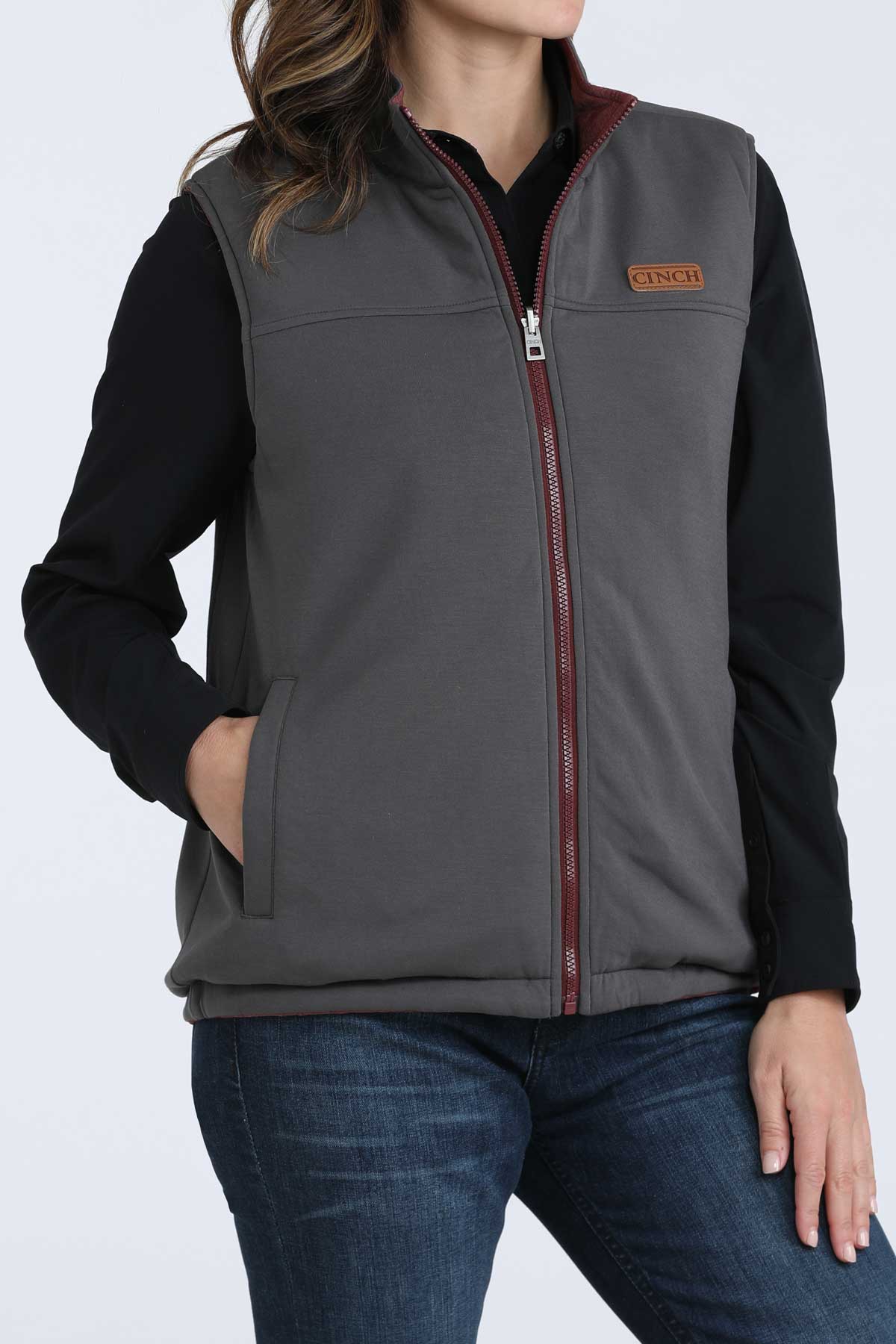 Woman wearing a gray vest with a black undershirt and jeans 