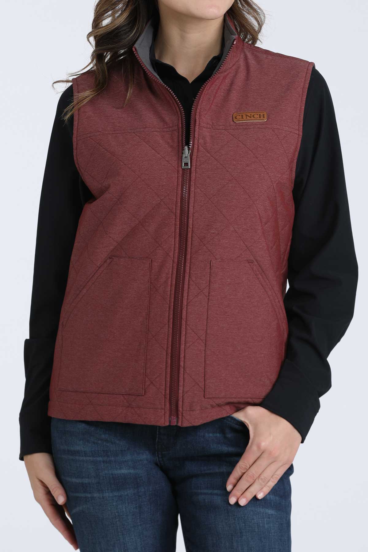Woman wearing a burgundy vest with a black undershirt and jeans 