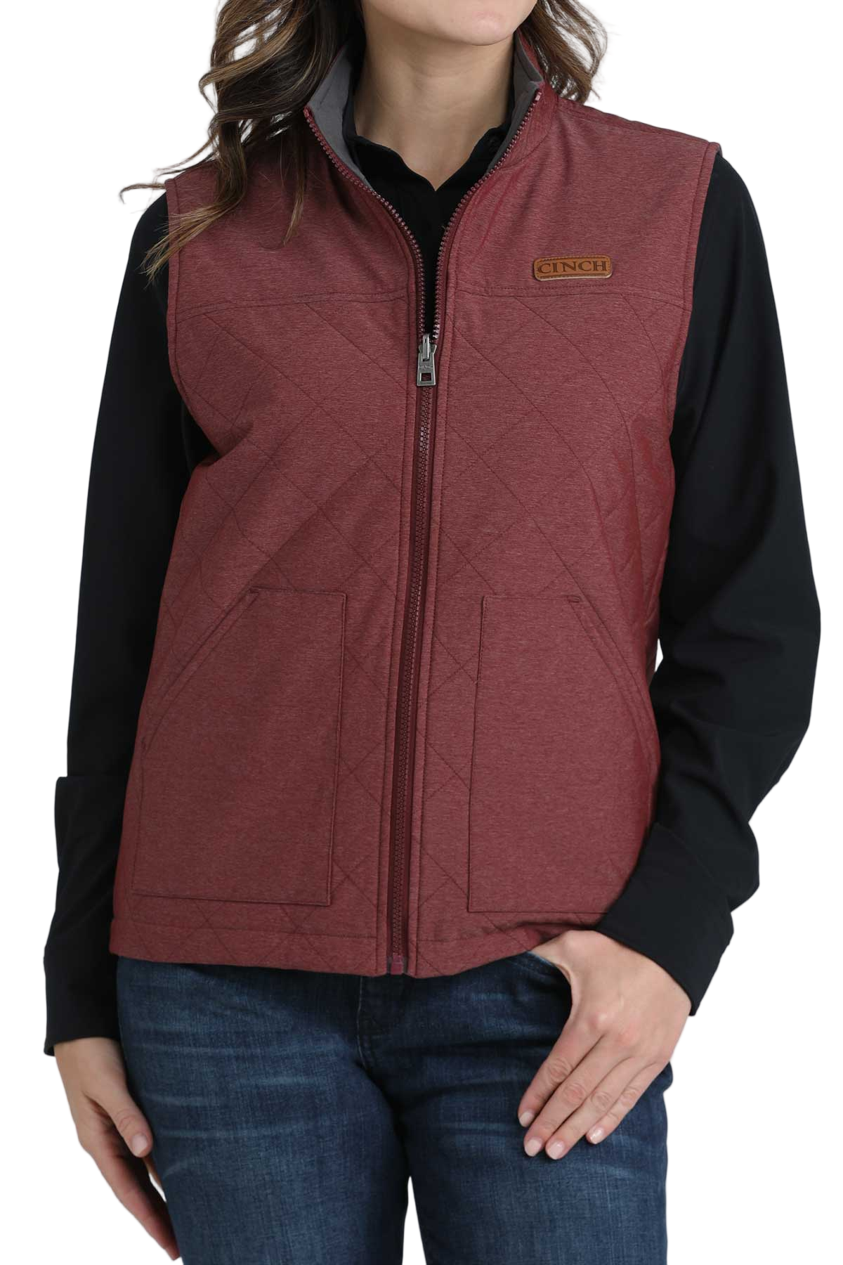 Woman wearing a quilted burgundy zip-up vest over a black long-sleeve shirt, paired with dark blue jeans.