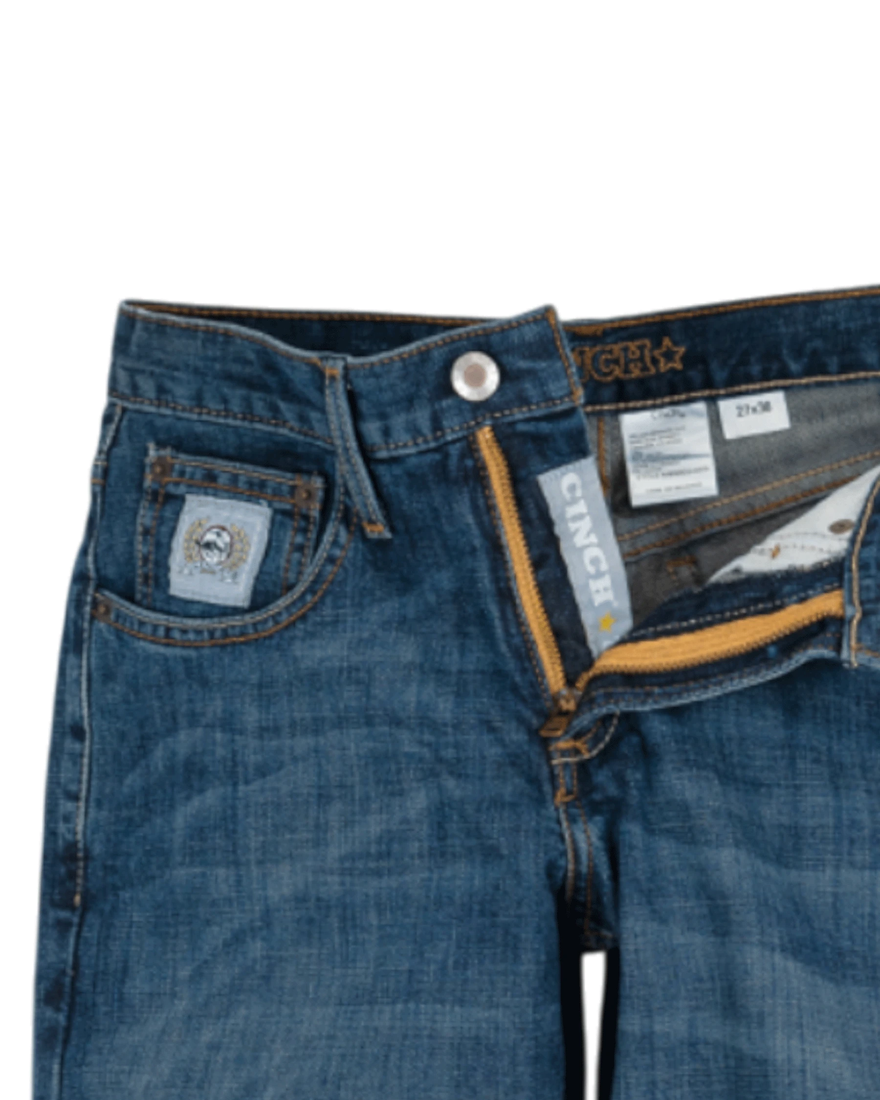 Close-up of the front of blue denim jeans with light fading, featuring a coin pocket with a small embroidered patch, belt loops, and a button closure with a zipper fly. The waistband has 'CINCH' stitched in gold thread