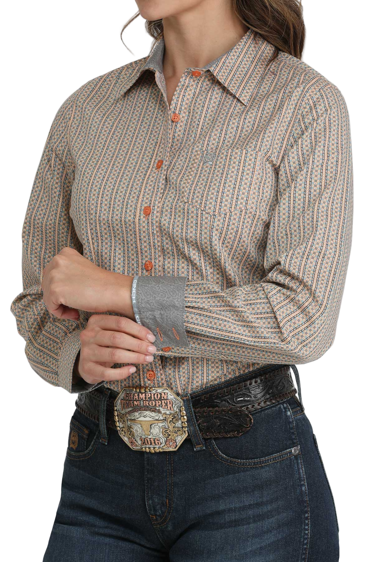 Woman wearing a brown striped button-down shirt with contrast cuffs, paired with dark blue jeans and a large silver western belt buckle