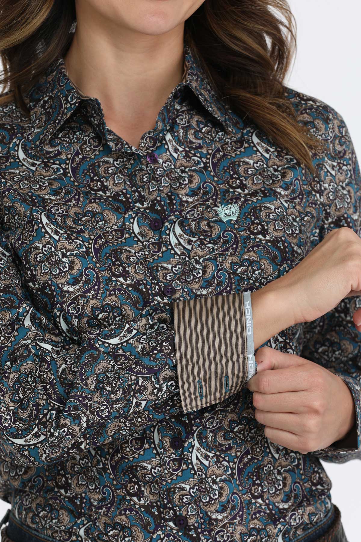 Woman wearing a dark paisley print button-up shirt with long sleeves, and contrasting cuff details
