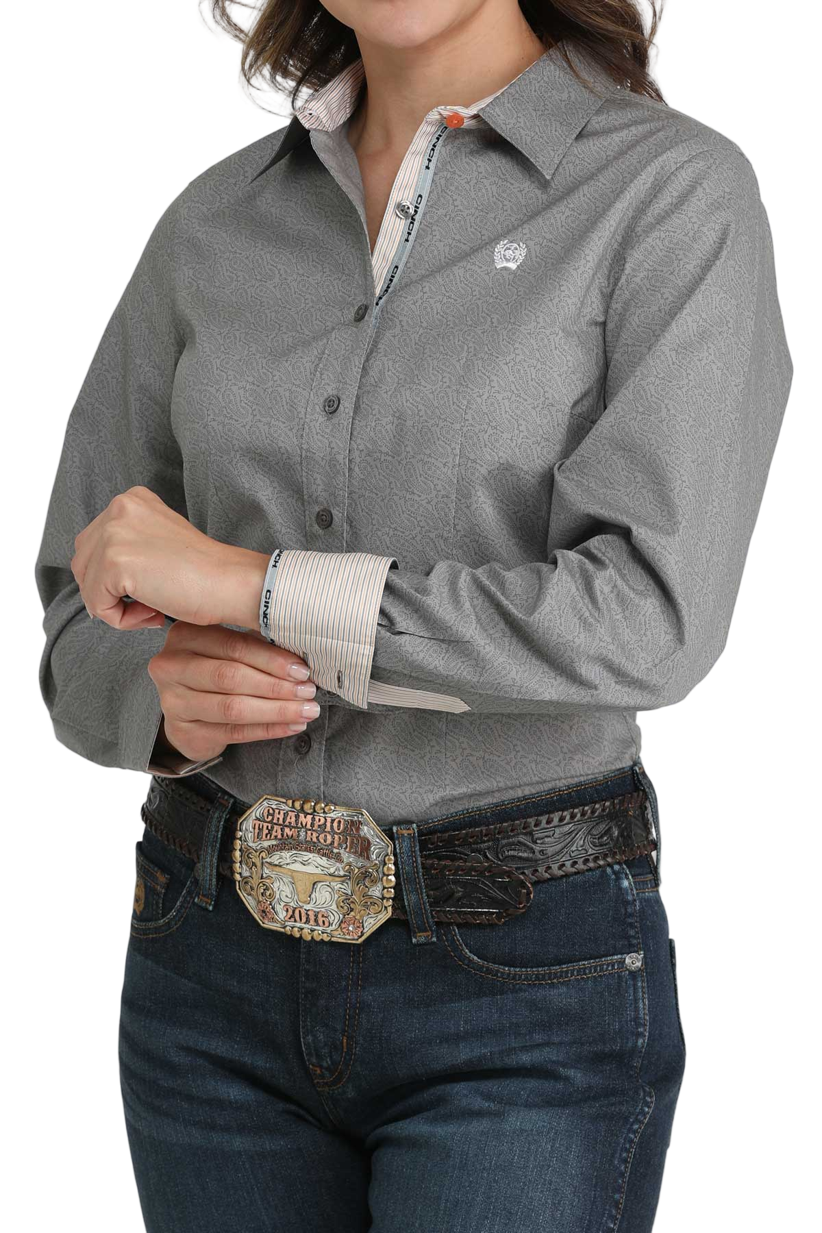 Woman wearing a gray long-sleeve button-down shirt with contrasting cuffs, paired with jeans and a large western belt buckle