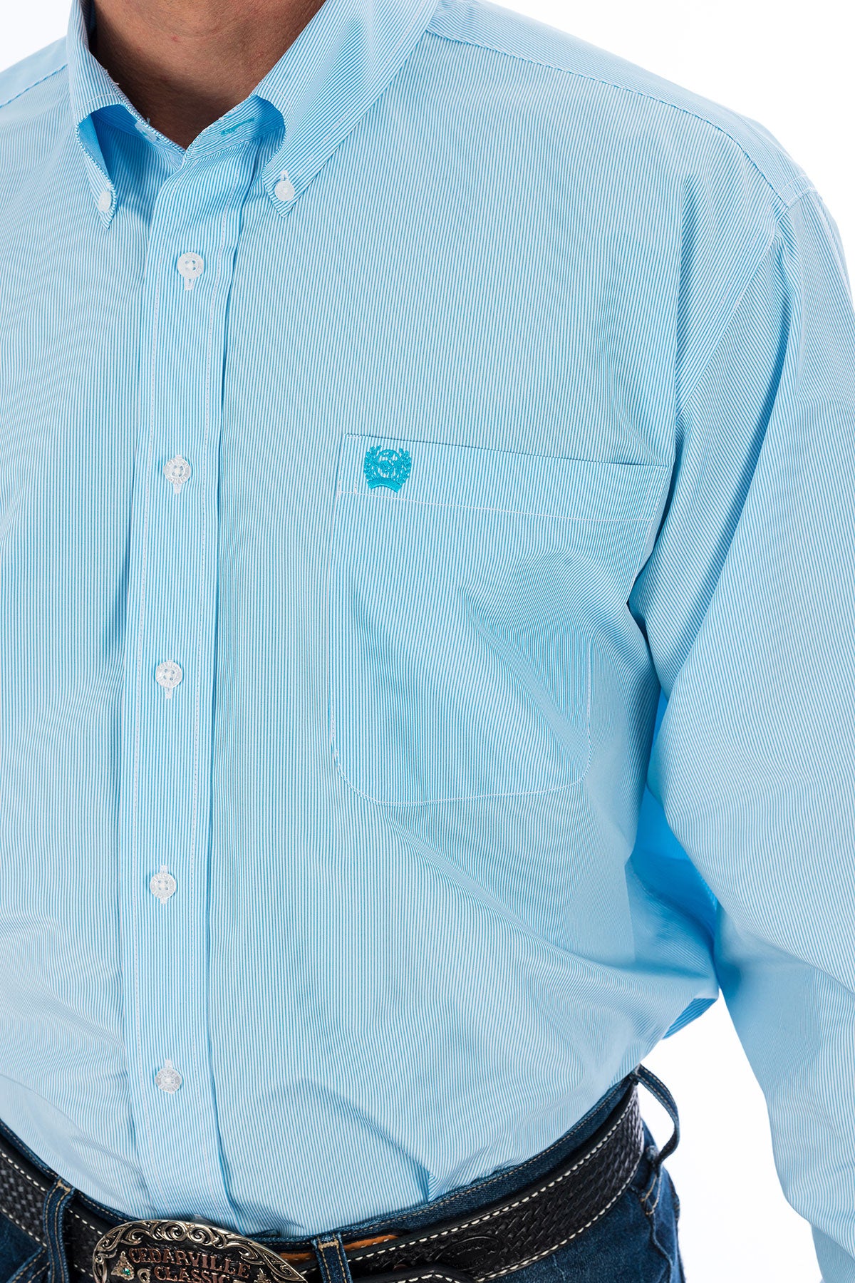 Man wearing a light blue, long sleeve, button-down shirt, with jeans and a western belt 