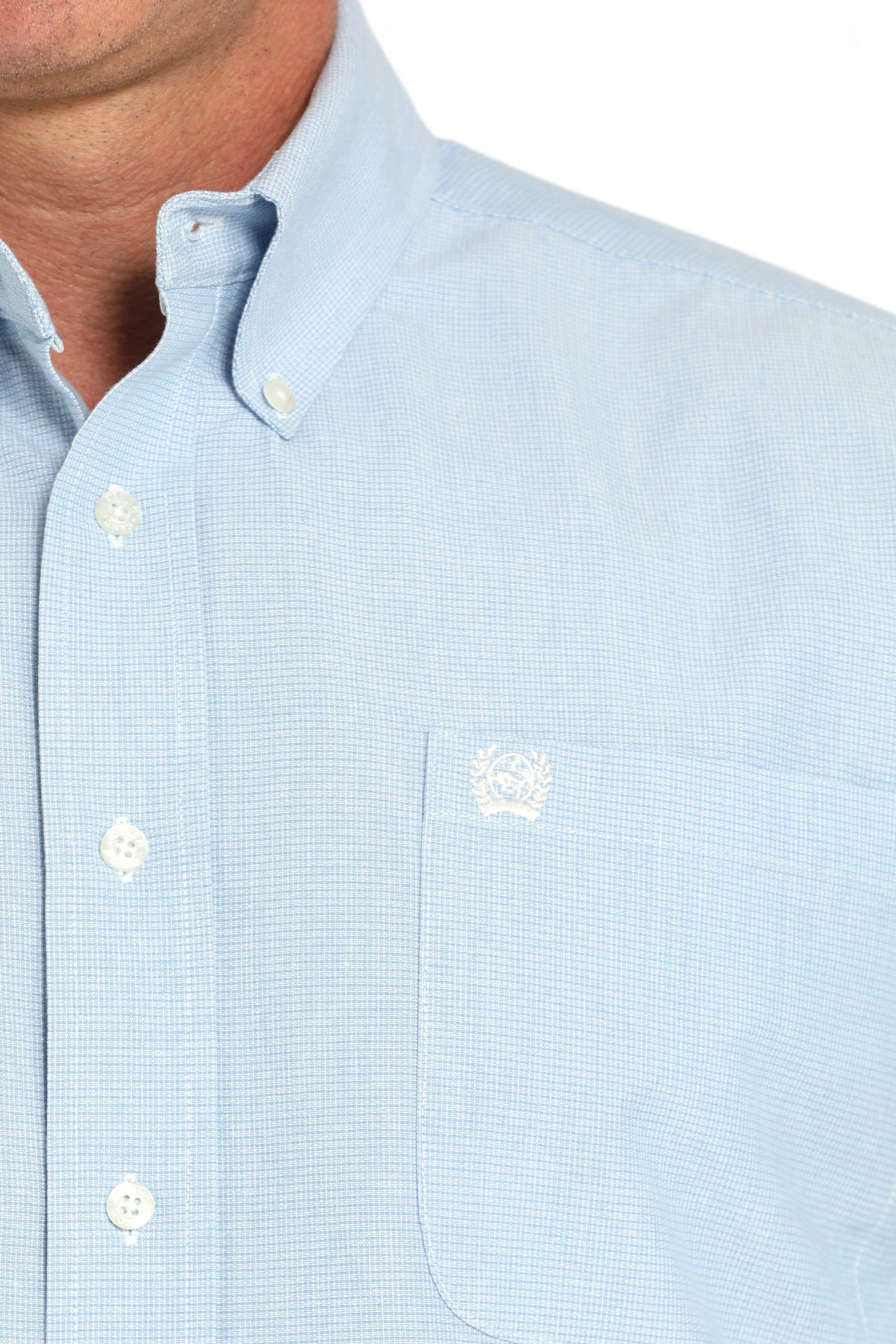 Close-up of a light blue shirt with a small logo on the chest pocket.