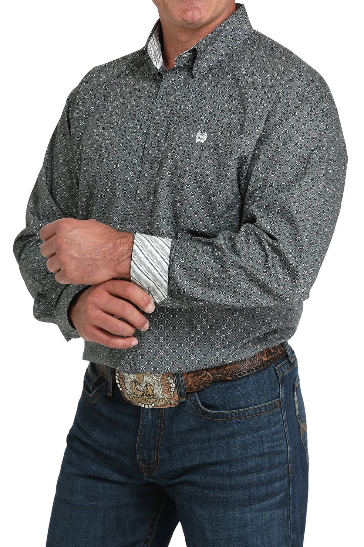 A man wearing a gray patterned button-up shirt with contrasting cuffs, dark jeans, and a large belt buckle, standing against a transparent background