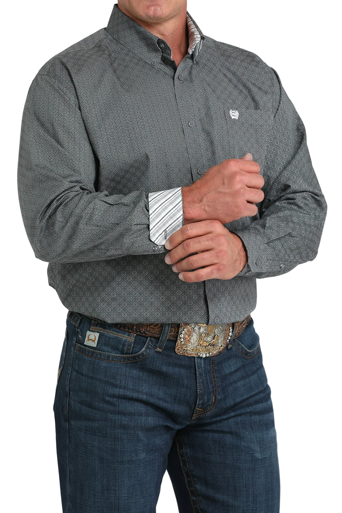 A man wearing a gray patterned button-up shirt with contrasting cuffs, dark jeans, and a large belt buckle, standing against a transparent background