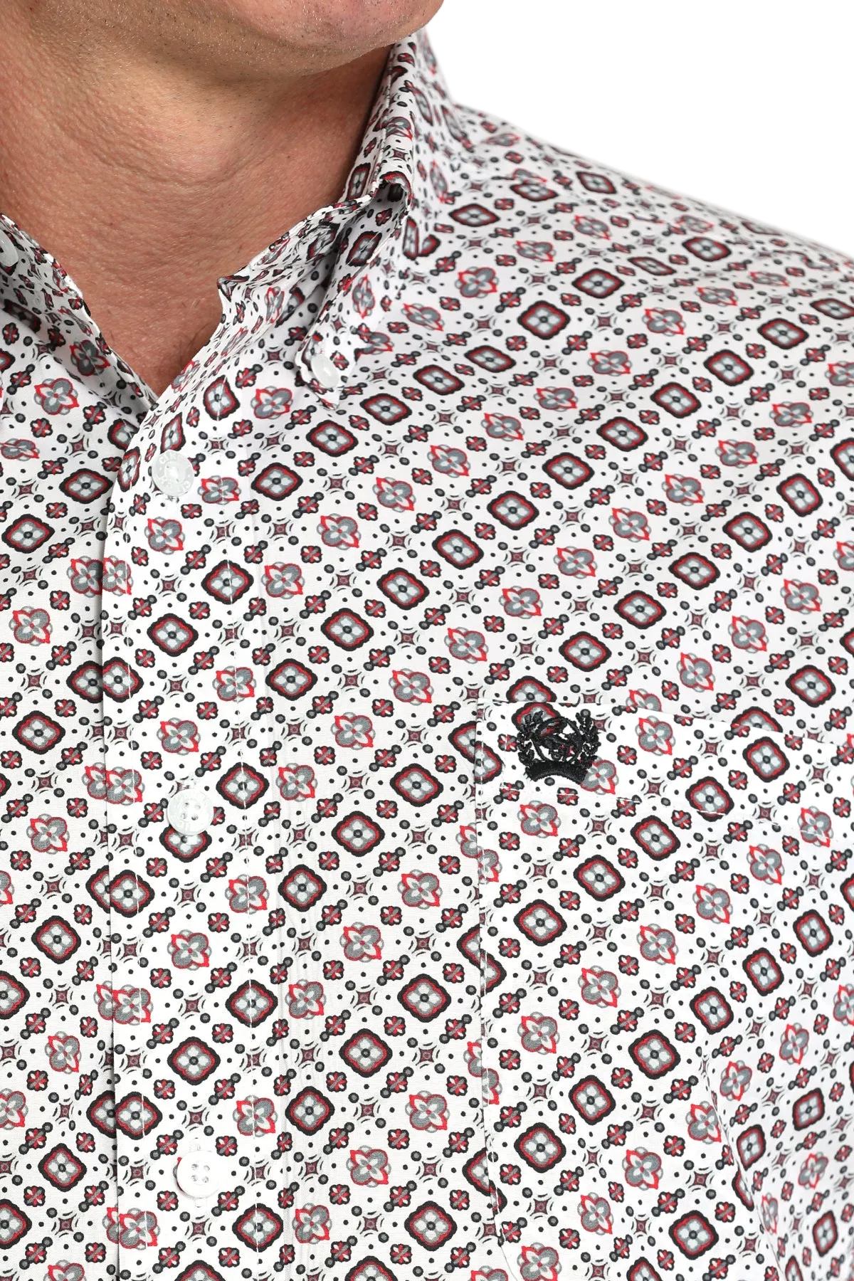 Close-up of a man wearing a light patterned button-up shirt with a small black emblem on the chest, displayed against a transparent background
