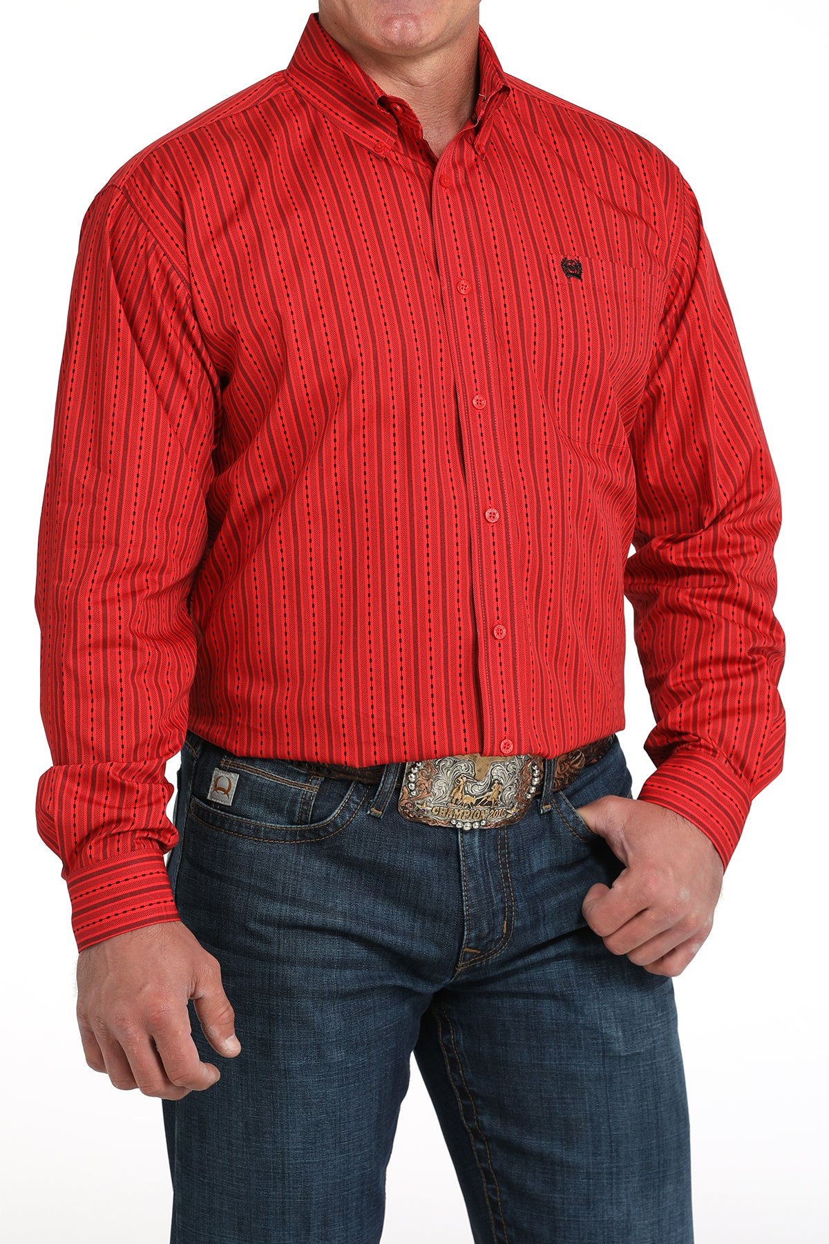 A man wearing a red striped button-up shirt, dark jeans, and a large belt buckle, standing against a white background
