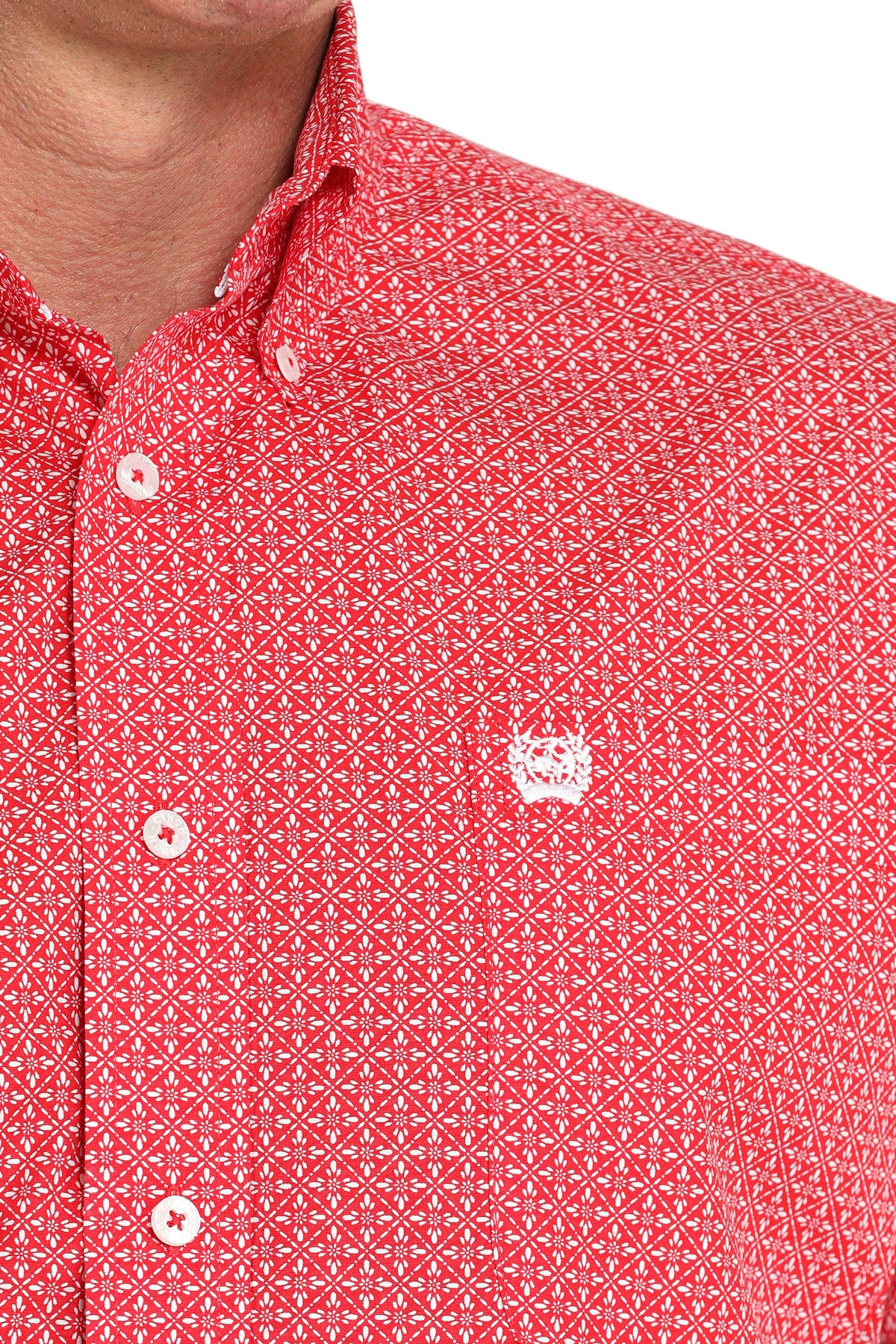 Close-up of a man wearing a red patterned button-up shirt with a small white emblem on the chest, displayed against a white background