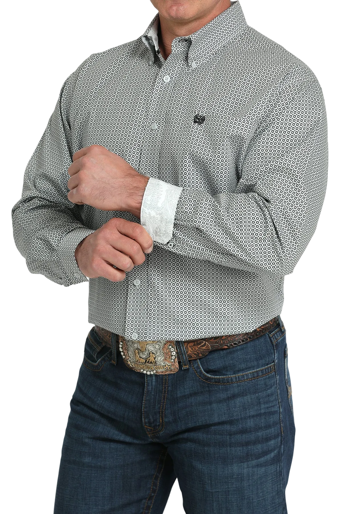 A man wearing a gray patterned button-up shirt with contrasting cuffs, dark jeans, and a large belt buckle, standing against a transparent background